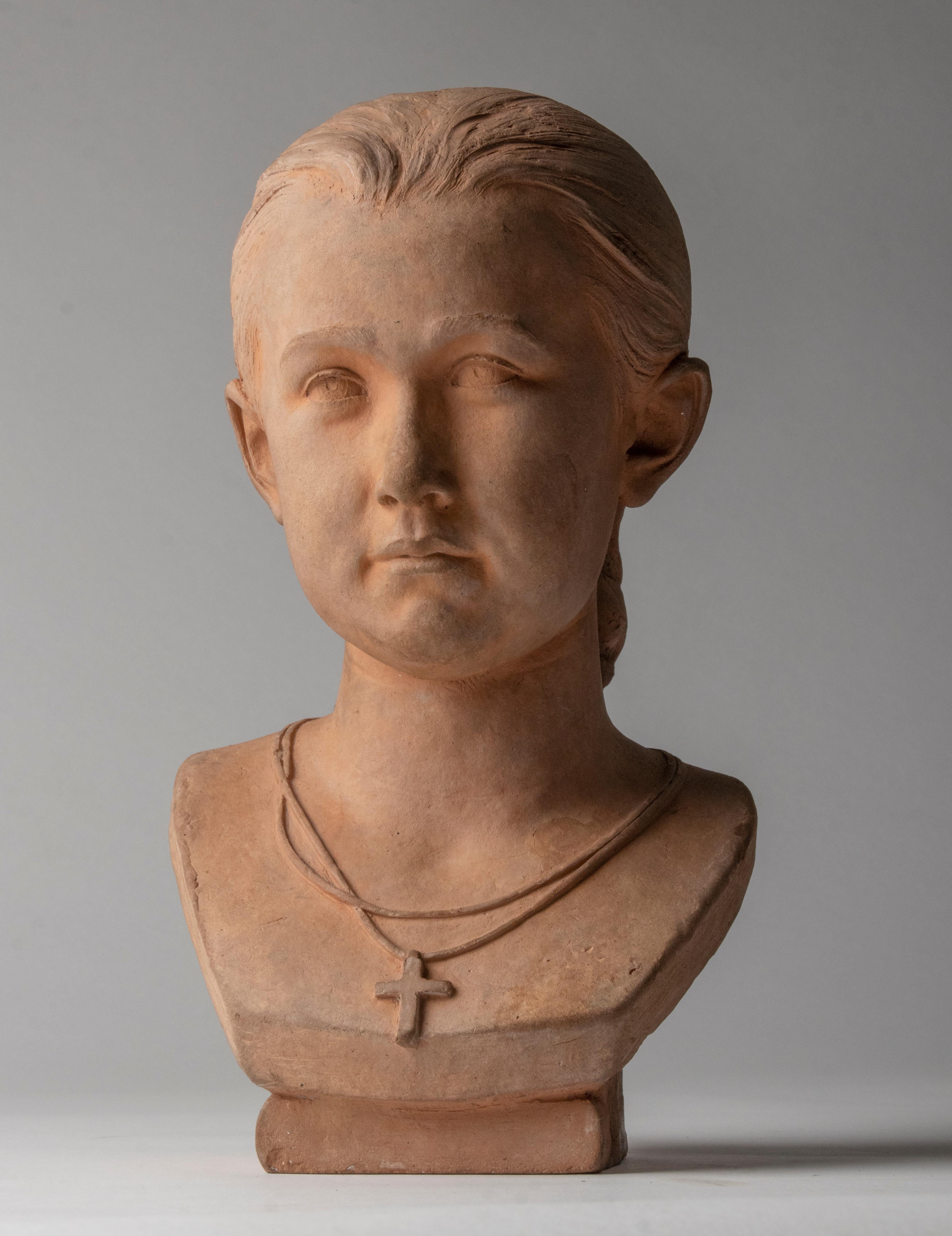 Beautiful antique sculpture by the French artist Jean Valette. The statue depicts a young girl, with a beautiful modest look and a Christian cross on a chain around her neck. The statue is made of terracotta, and has a beautiful antique
