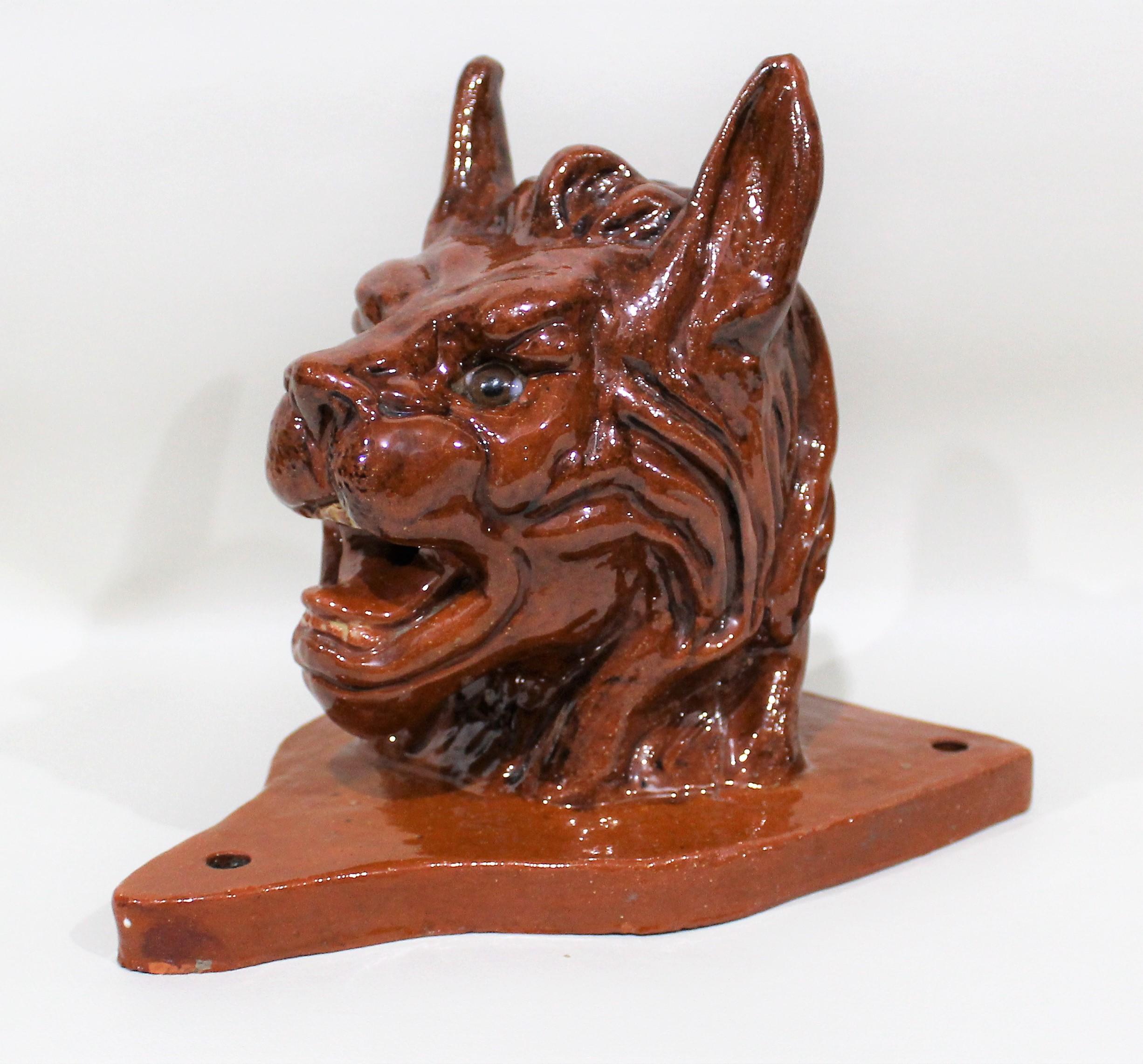 19th century terracotta figural font modeled as the head of a mythical feline with glass eyes. It's mounted to a crest form back.