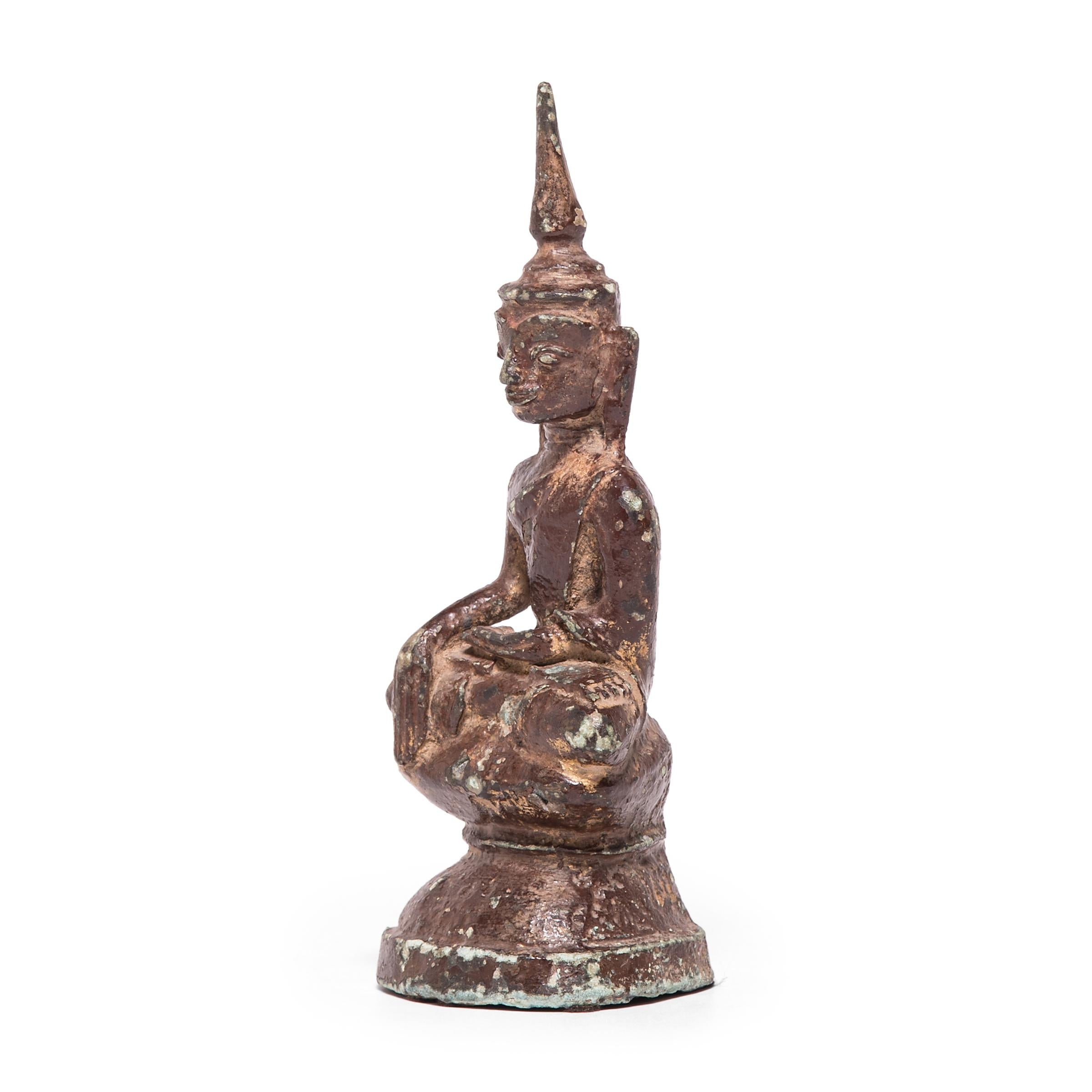 This serene Buddha figure was cast in bronze by a Thai artisan over a century ago.The flame-like spike stretching upward from the crown of his head is called an ushnisha—it signifies wisdom, and is one of the 32 marks of the Buddha’s greatness. Many