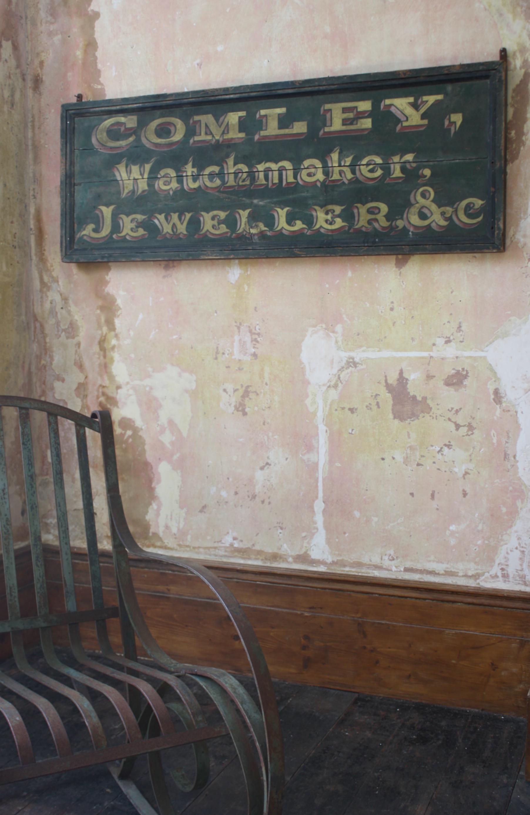 A pretty much perfect late 19th century trade sign, a dark green ground with a pale pink and yellow elaborate front. 

The trade sign we believe is from Somerset, Bath circa 1890 and relates to a Thomas Comley who was a watchmakers and jeweller.