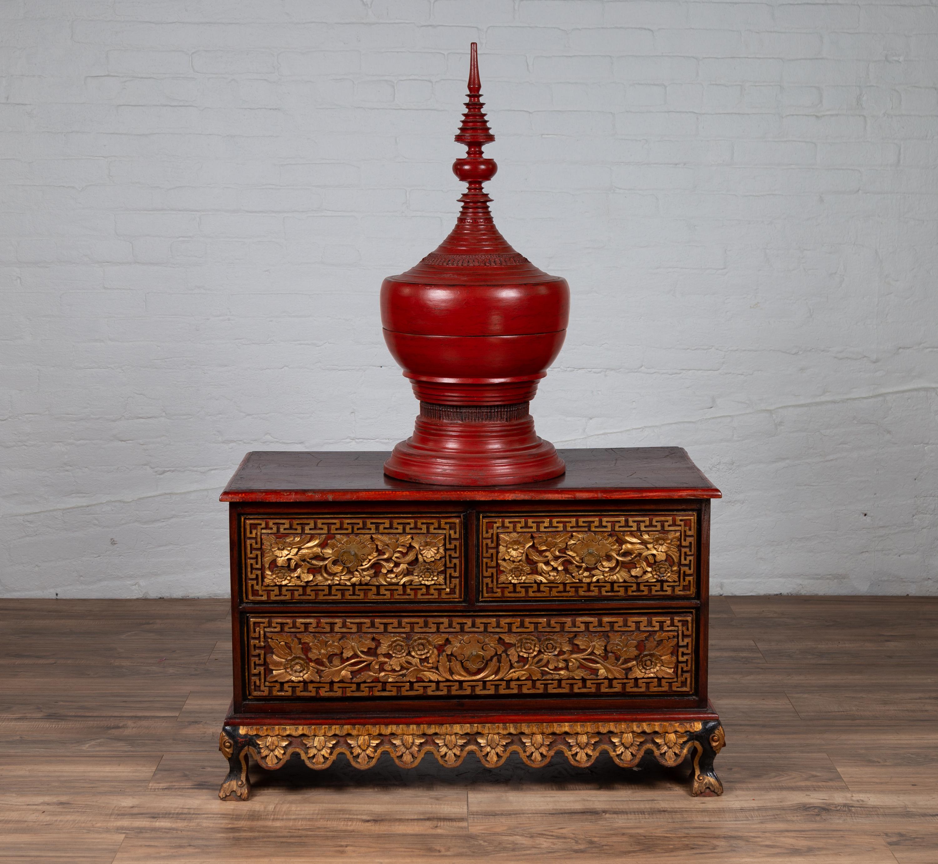 An Indonesian wooden three-drawer dresser from Madura with richly carved giltwood floral and Meander motifs, and red and brown patina. Born in Madura off of the northeastern coast of Java during the 20th century this exquisite chest captures our