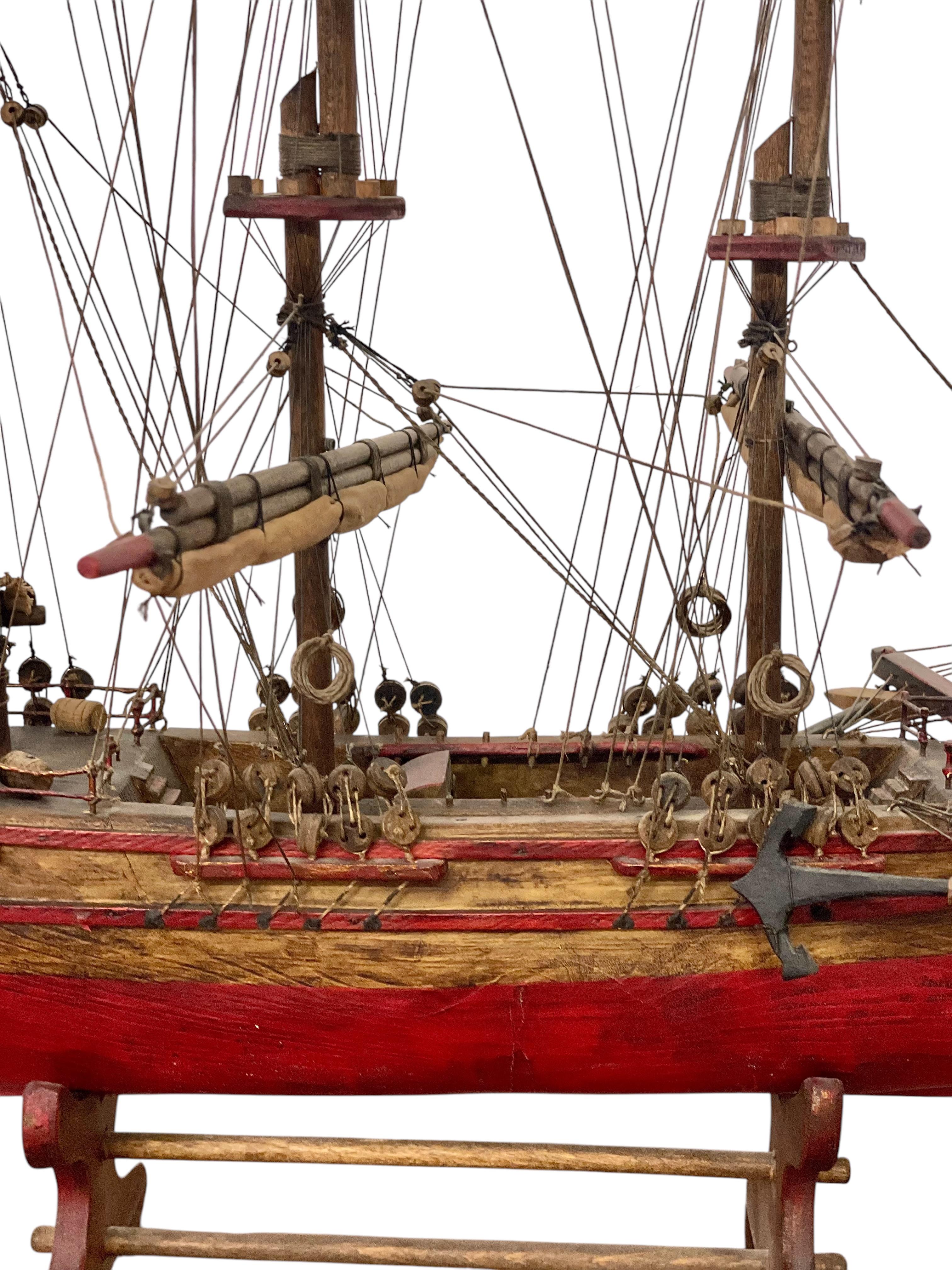 Cette exquise maquette de bateau en bois, méticuleusement réalisée, est une représentation étonnante d'un voilier à trois mâts. La coque est peinte d'un cramoisi profond avec des accents de bois naturel et des détails complexes tels que des canons