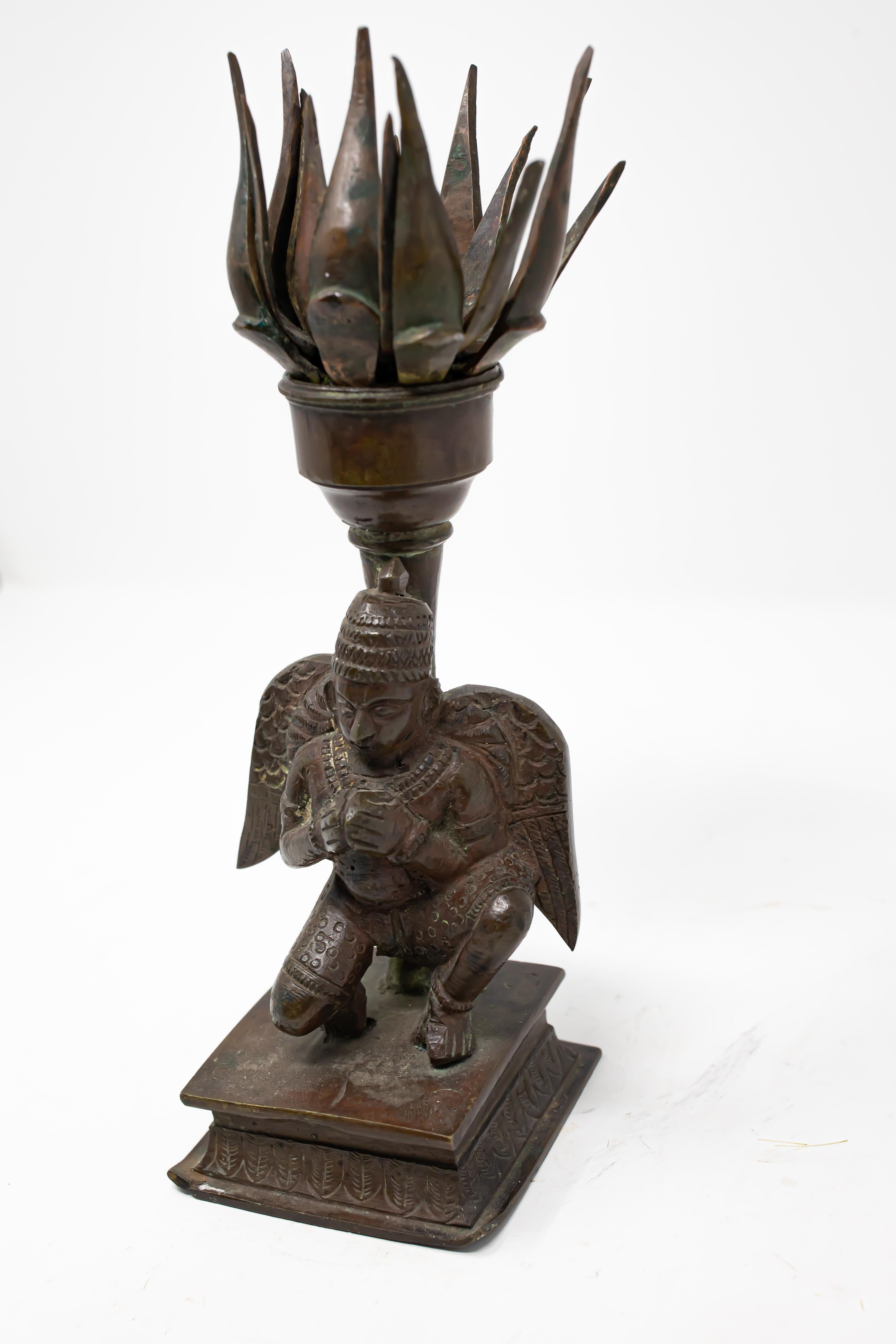 Offering this unique bronze Tibetan censer from the 19th century. Starting on a square base with foliate designs that go around in a center band. It rises to a figure that is kneeling and has wings. Behind him is a stem that rises to a Lotus flower