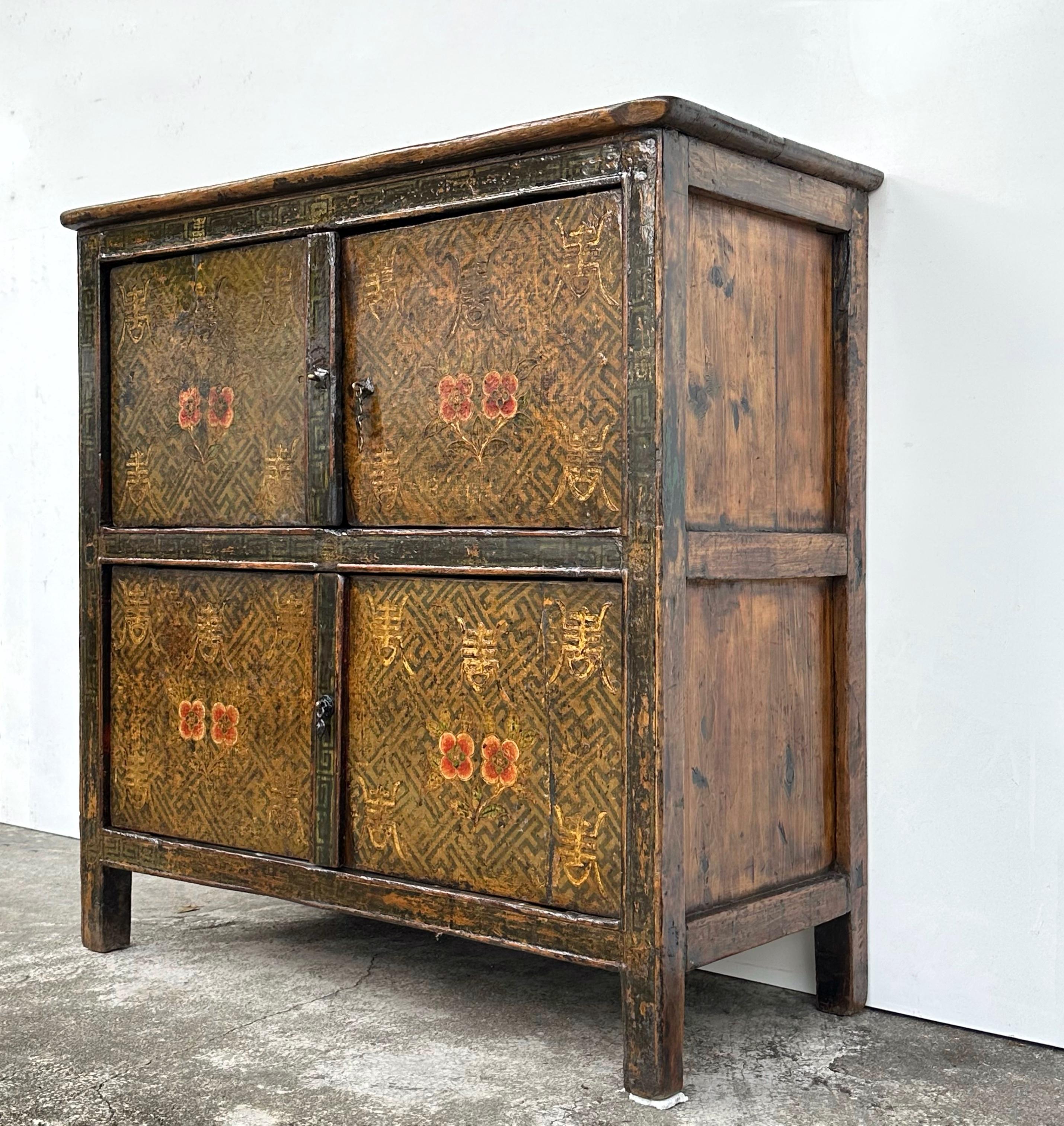 A beautiful Tibetan cabinet with subtle hand-painted designs, there is a pair of small red flowers on each door, and each pair of flowers is accompanied by five longevity symbols (painted in white). These designs are painted over a Buddhist swastika