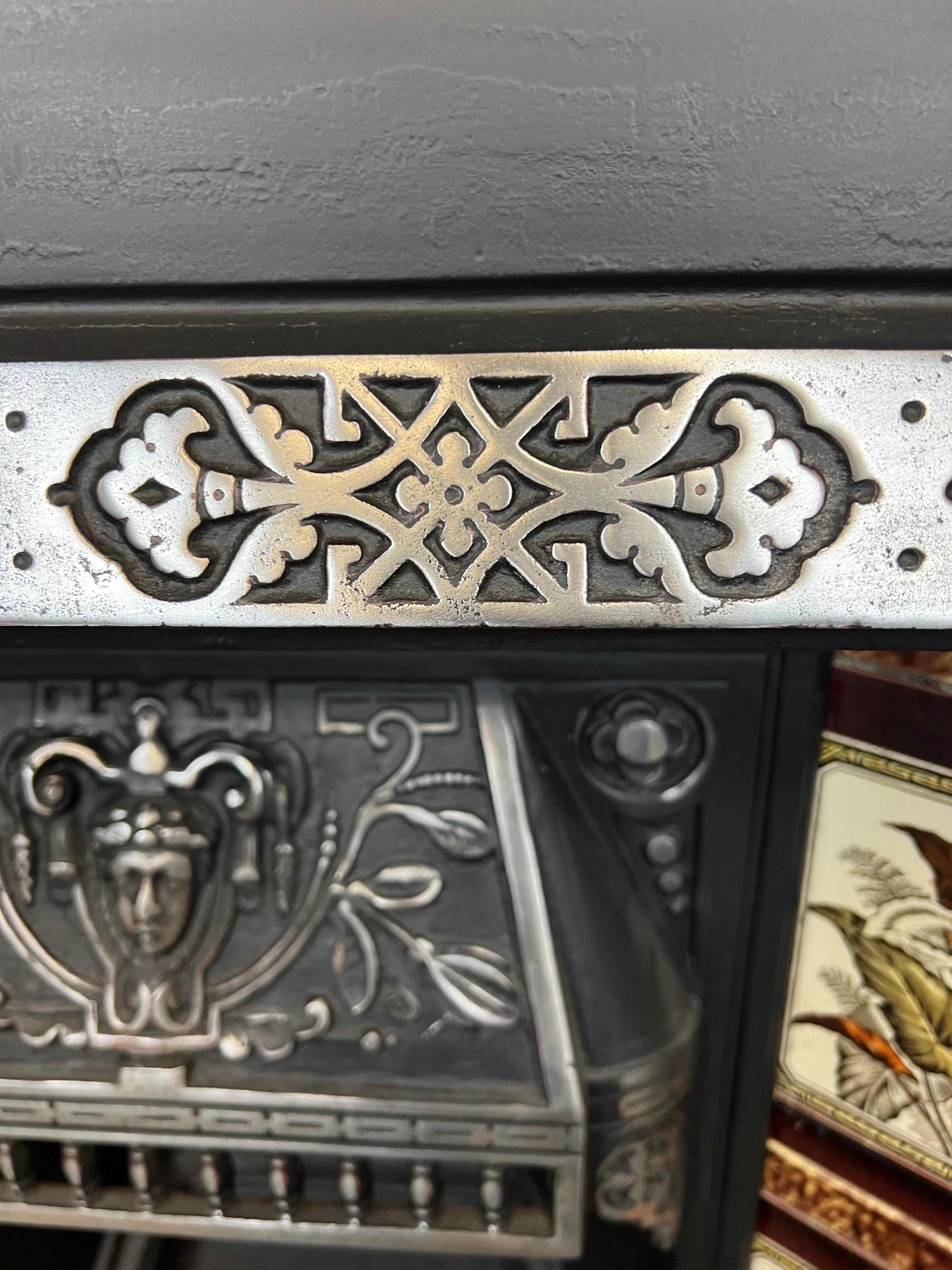 19th Century tiled cast iron fireplace insert.
A fine example of English Victoriana. Made in England circa 1880.
Burnished relief to the decorative hood showing boy face & foliage, bars and patterned trim with blackened finish to fire back and