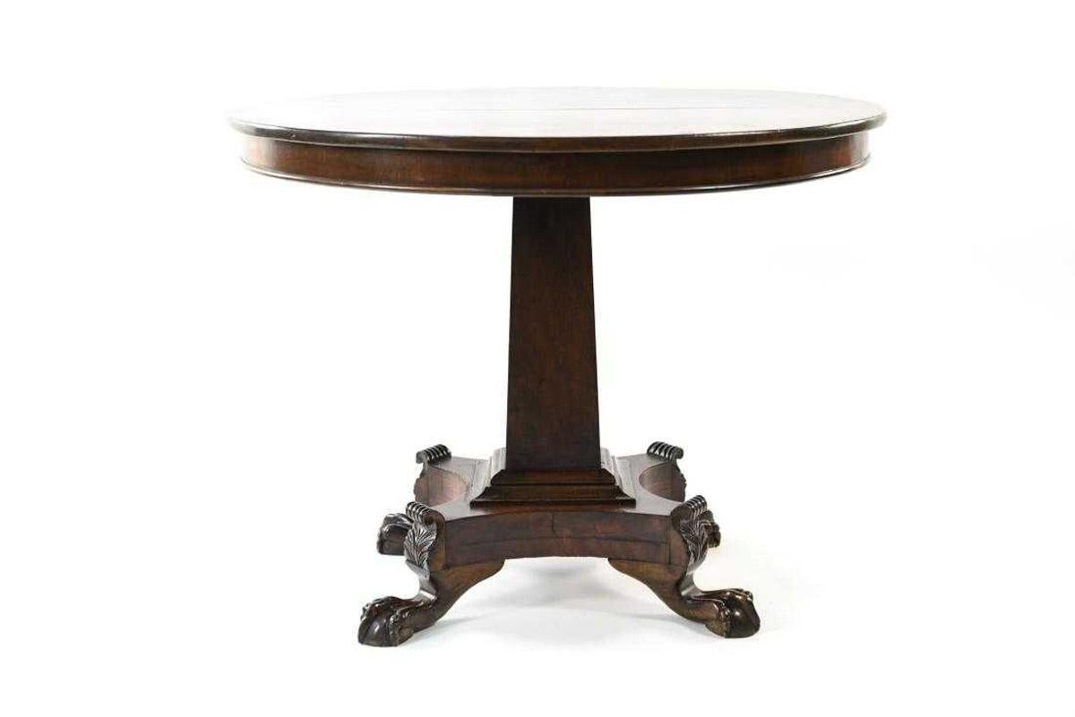 The early 19th century English Regency rosewood round tilt-top table has a square centre pedestal supported by four hand carved ball-in-claw feet. Acanthus leaves are seen above the feet. Works well as an elegant card, small dining, tea, breakfast