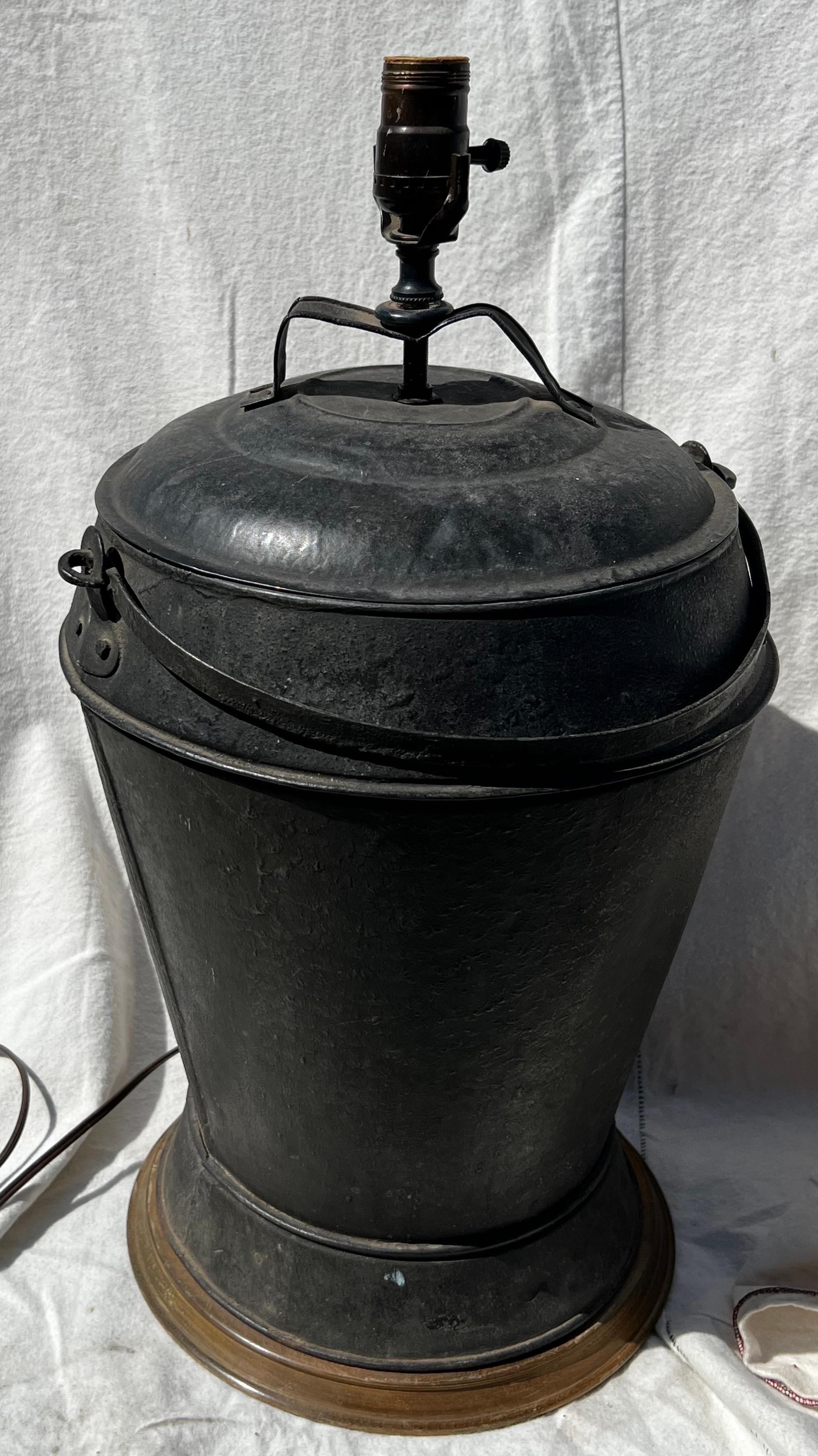 19th century tin bucket with swing handle, in black paint, converted to lamp, with wooden base. Old dent to top and slight bend in socket mount.