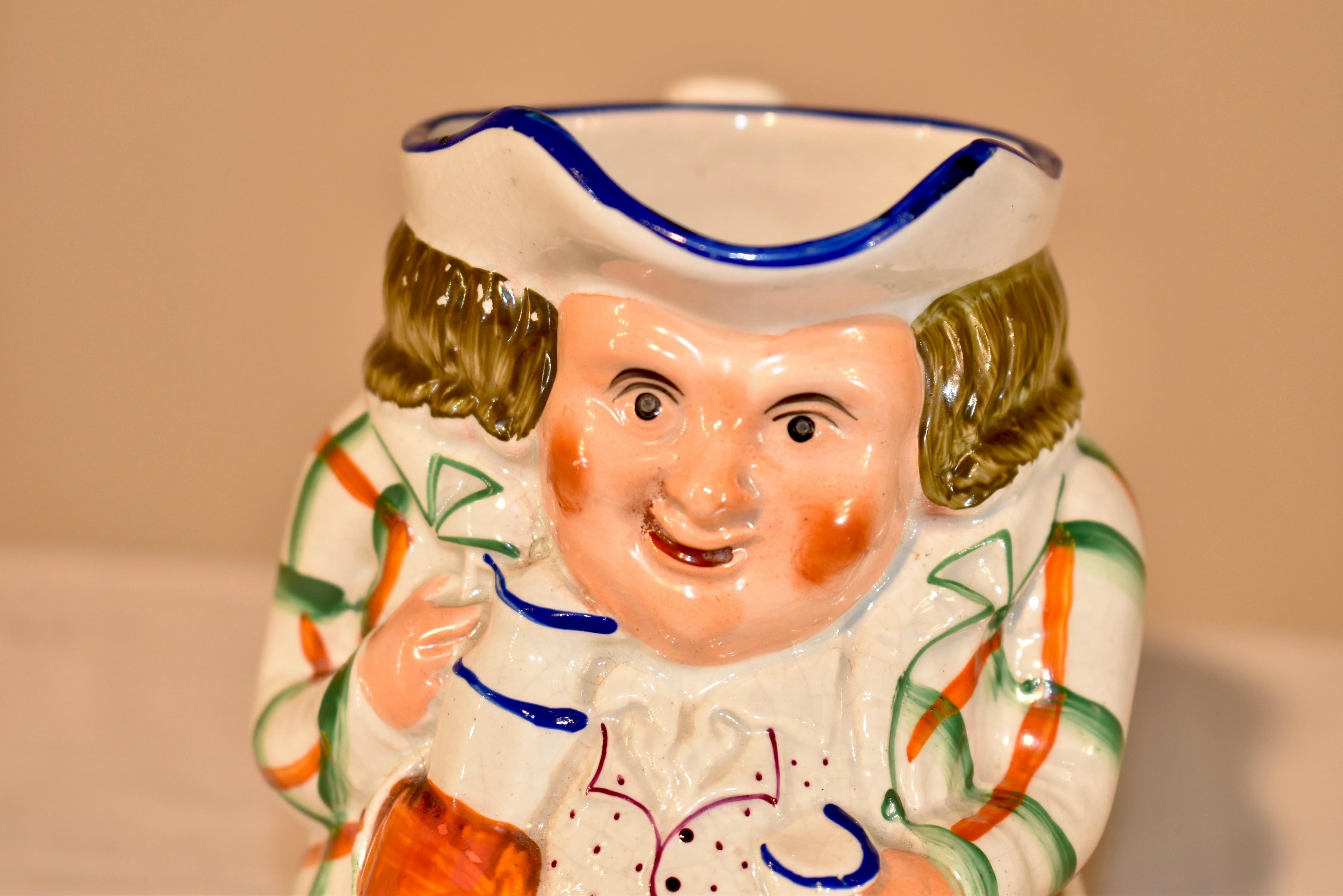 19th century ceramic Toby jug from the Staffordshire region of England.  He has a lovely plaid jacket and polka dotted vest.  He wears a warm expression on his face.  