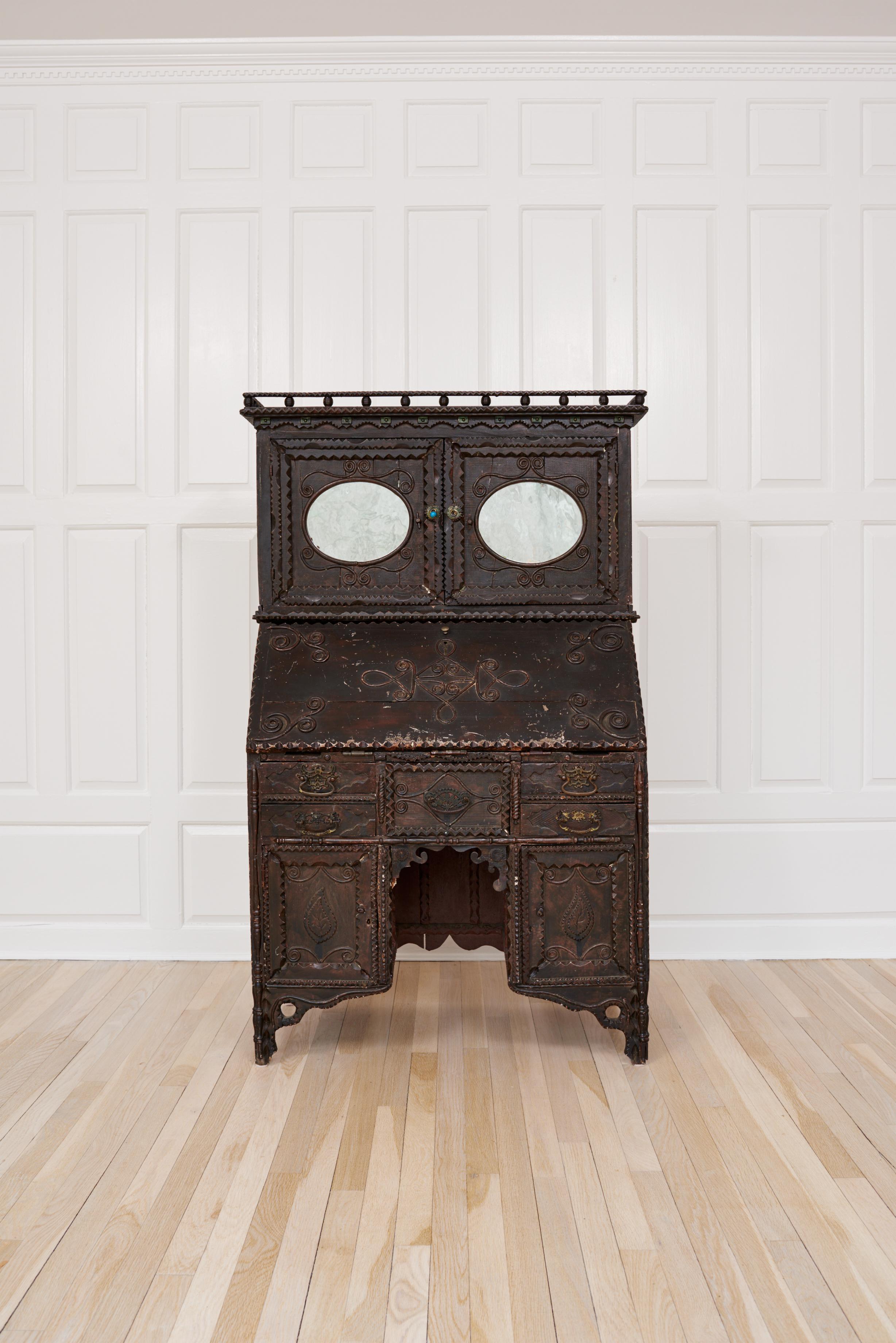 19th century. Southampton, New York. Tramp Art desk decorated with applied reed scrolls and tramp carving. Galleried top with two oval mirrored doors. Doors have wood mechanical locking mechanism, opening to a fitted interior, set on a slant front