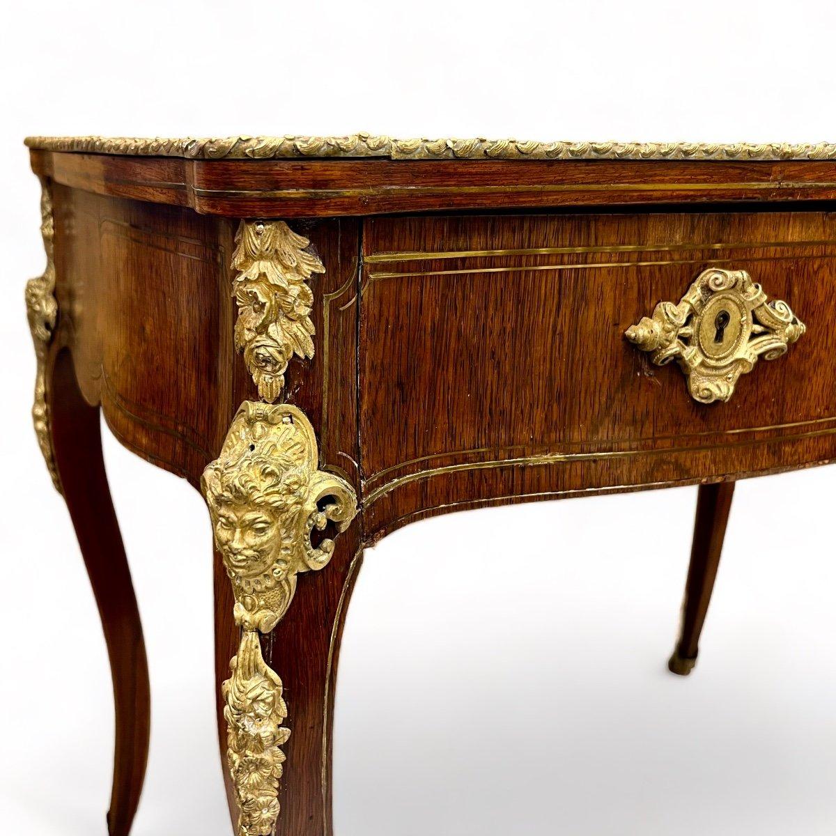 Ce petit bureau du XIXe siècle est réalisé en bois de rose avec des filets de laiton insérés. Il présente un mélange transitoire d'éléments représentatifs des styles Louis XV et Louis XVI, notamment dans ses pieds courbés. Les pieds et le tablier du