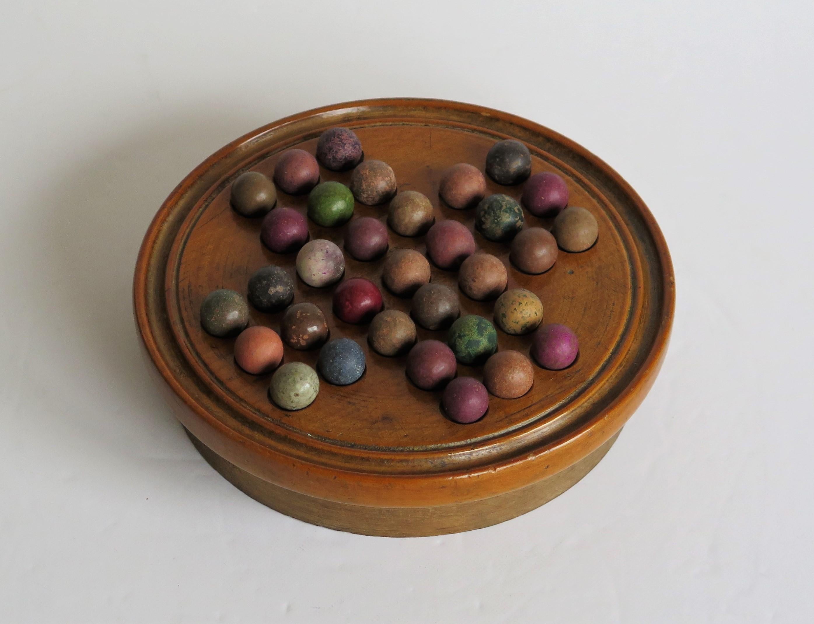 This is an original and complete game of travelling marble solitaire from the 19th century with 33 old clay and stone marbles, circa 1870.

This two-piece board has a fairly small diameter and is unusual in that it has a circular open wood base