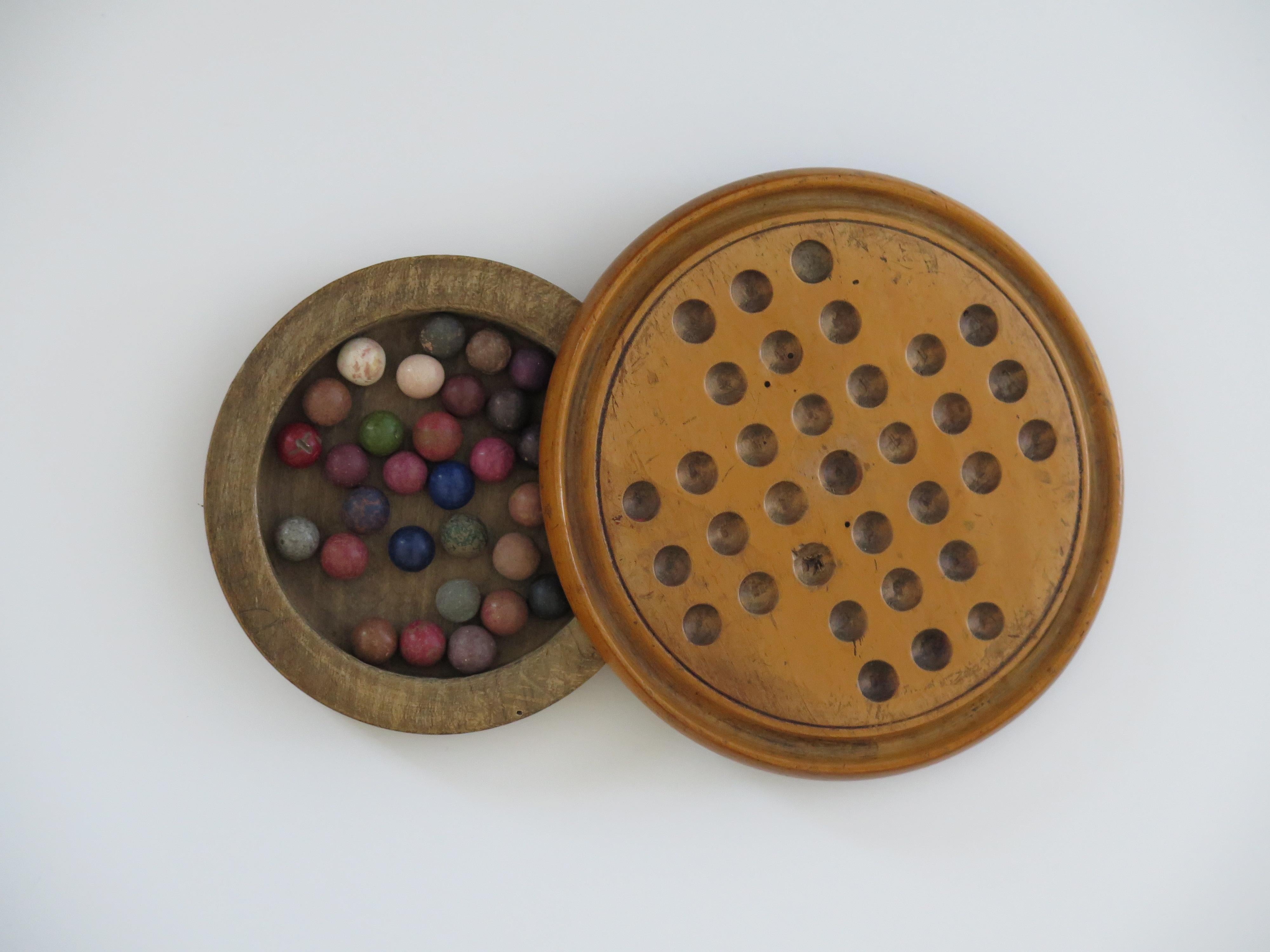 This is an original and complete game of travelling marble solitaire from the 19th century with 33 old clay and stone marbles, circa 1870.

This two-piece board has a fairly small diameter and is unusual in that it has a circular open wood base