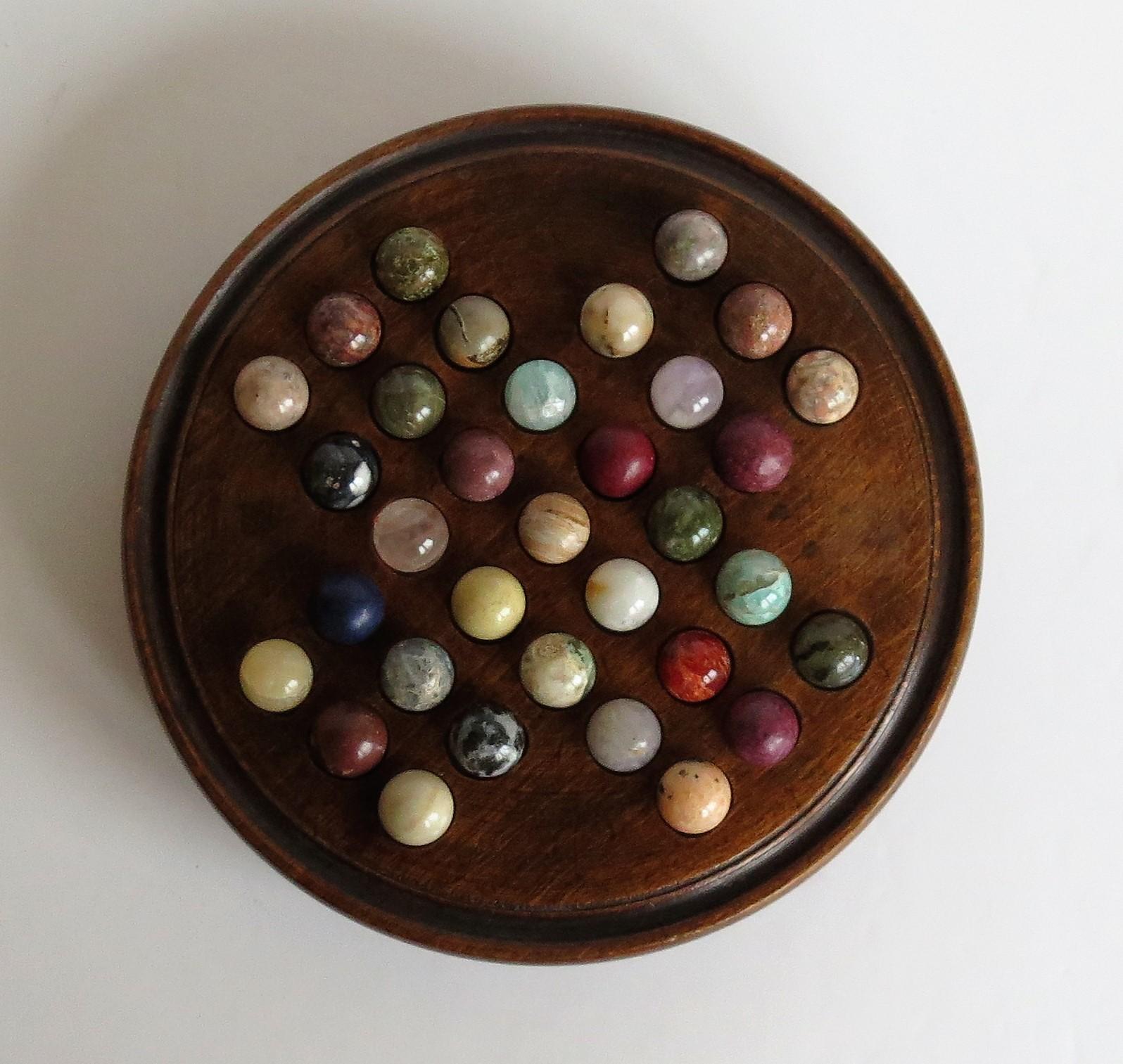 This is a very attractive complete game of travelling marble solitaire with 33 beautiful agate mineral stone marbles, from the late 19th century.

This two-piece board has a fairly small diameter of less than 6 inches and is unusual in that it has