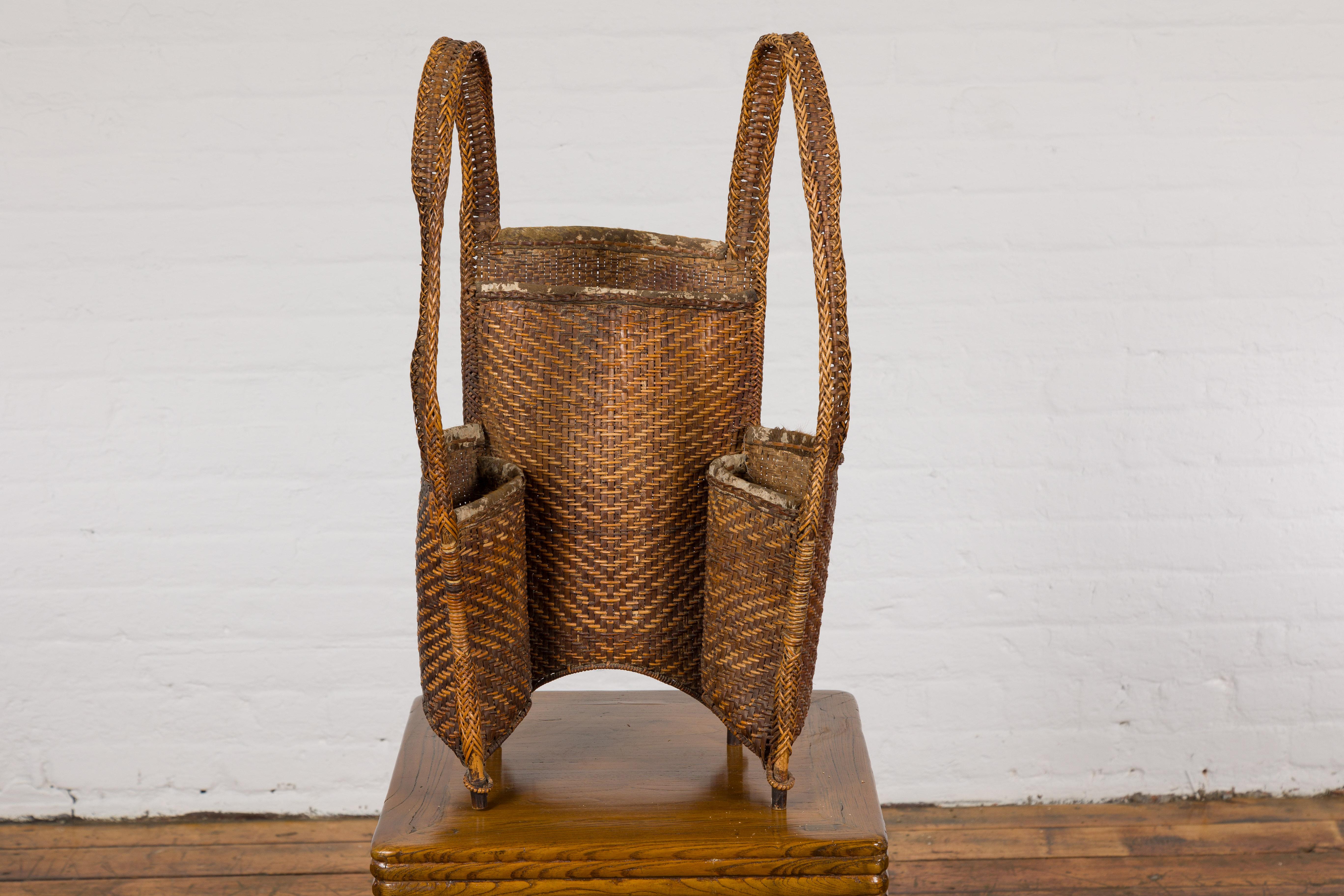 An antique hand-woven rattan backpack with three inner pockets and rustic character. Experience a slice of Thailand's rich cultural history with this unique antique hand-woven rattan backpack. Designed with practicality and aesthetics in mind, this