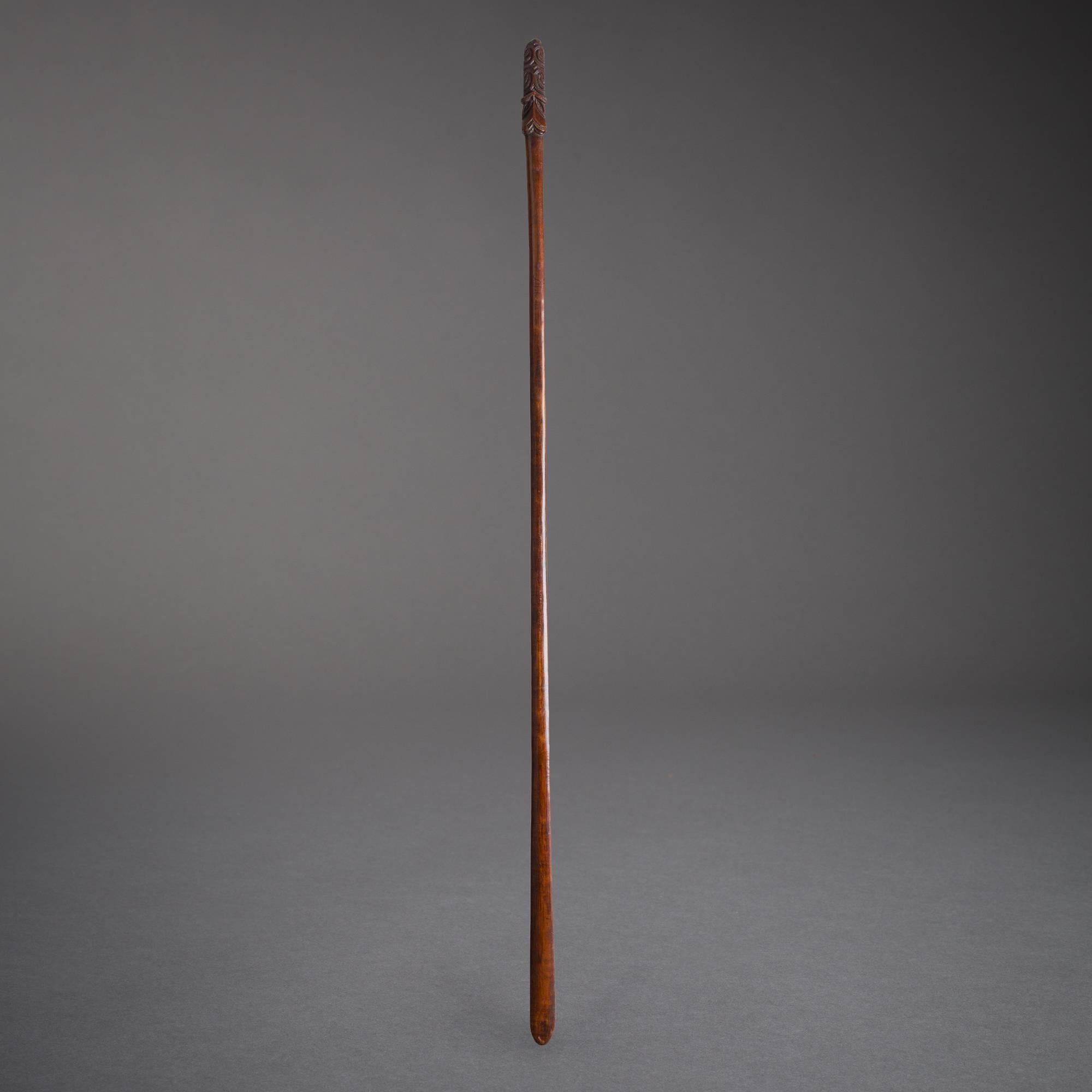 A traditional Maori staff (taiaha), carved from a single piece of hardwood and endowed with a deep, warm patina of age. The 'tongue' of the staff (arero), used to deliver stabbing blows and sharp strikes, is meticulously carved with swirling motifs