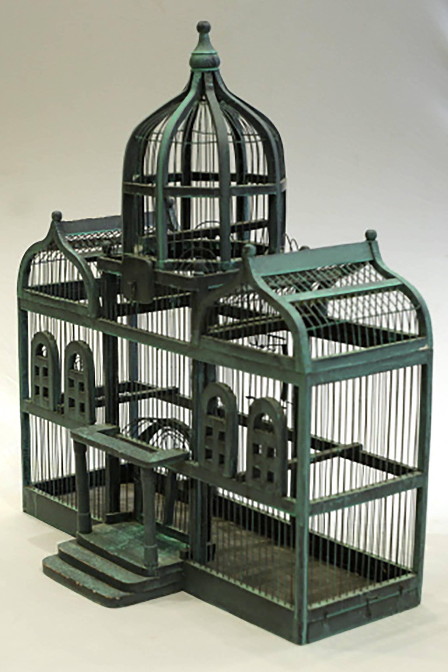 Painted wood and wire Victorian bird cage with three domes, a front porch, one door in the front and one in the back. The bottom has a metal tray and there are three perches inside for a bird to rest on. 

Measures: 31.5 H, 14 D 27.5.
