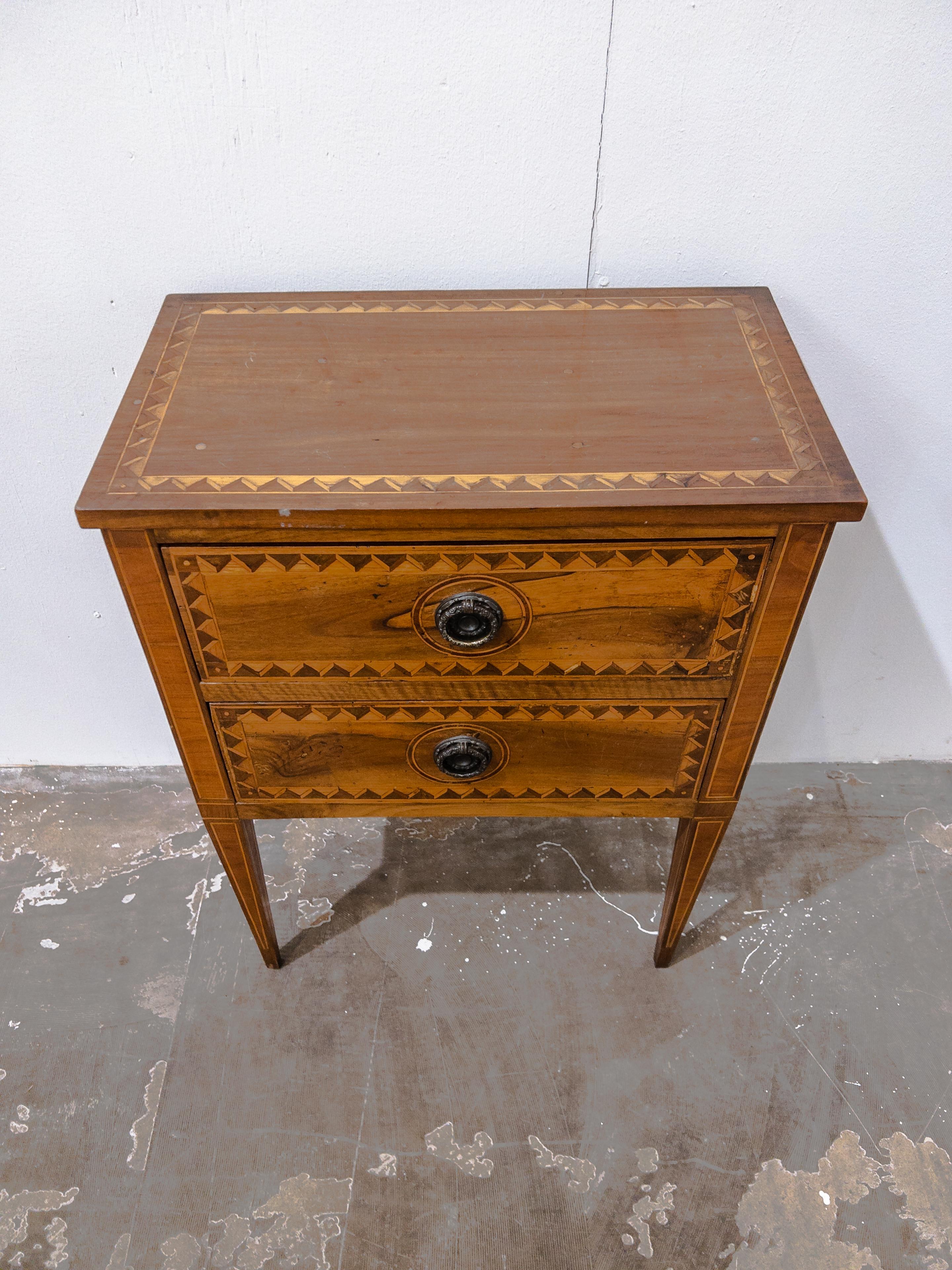 A testament to the artistry of the 19th century, the Two Drawer Small Fruitwood Commode with Marquetry Detail exudes timeless beauty and intricate craftsmanship. Crafted with meticulous attention, this commode showcases the rich allure of fruitwood,
