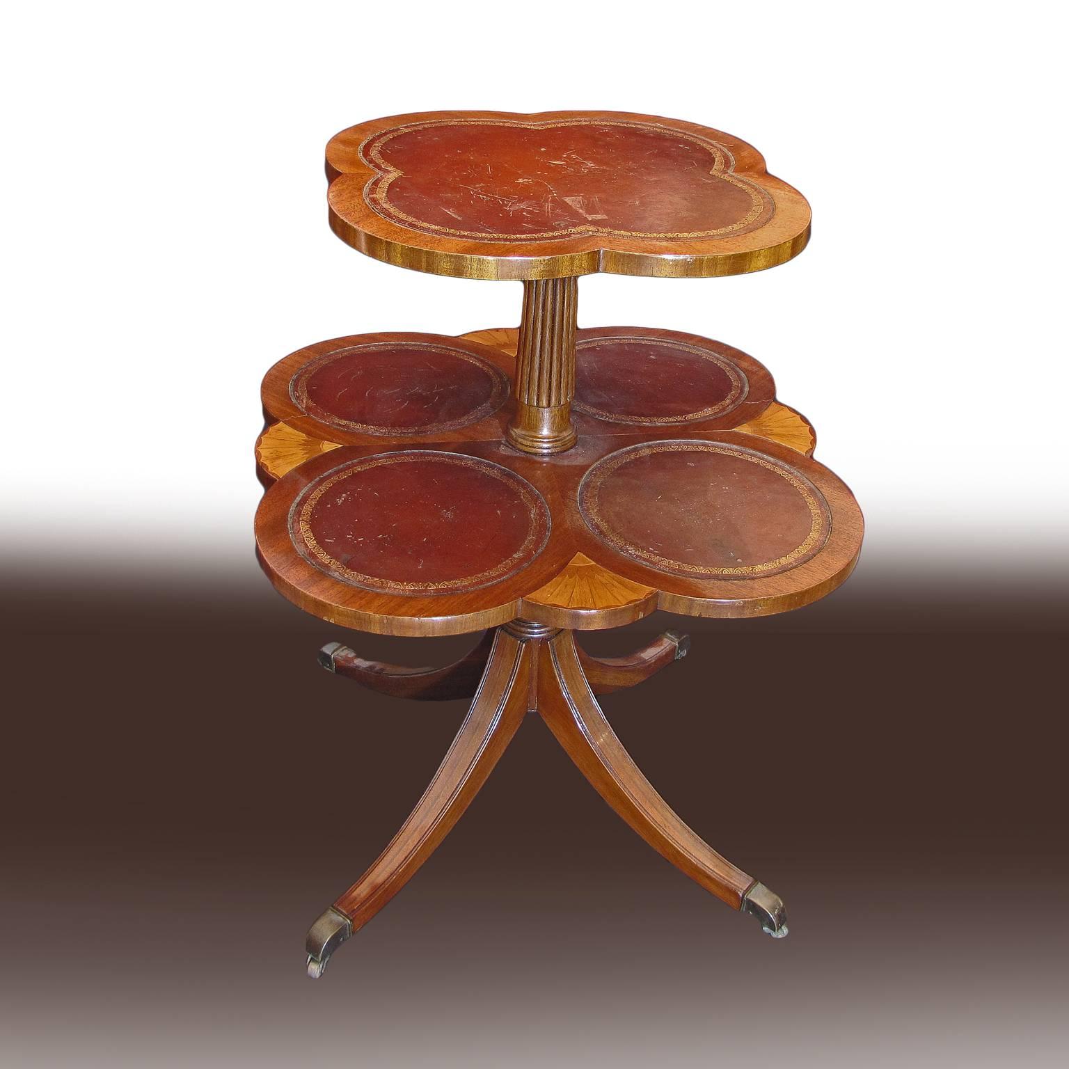 A beautiful pair of typical English style two-tier side tables in mahogany wood, with a beautiful leather lined quatrefoil tabletop and veneered Rosewood details. The tables rest on a central column of mahogany wood, which is supported by four saber