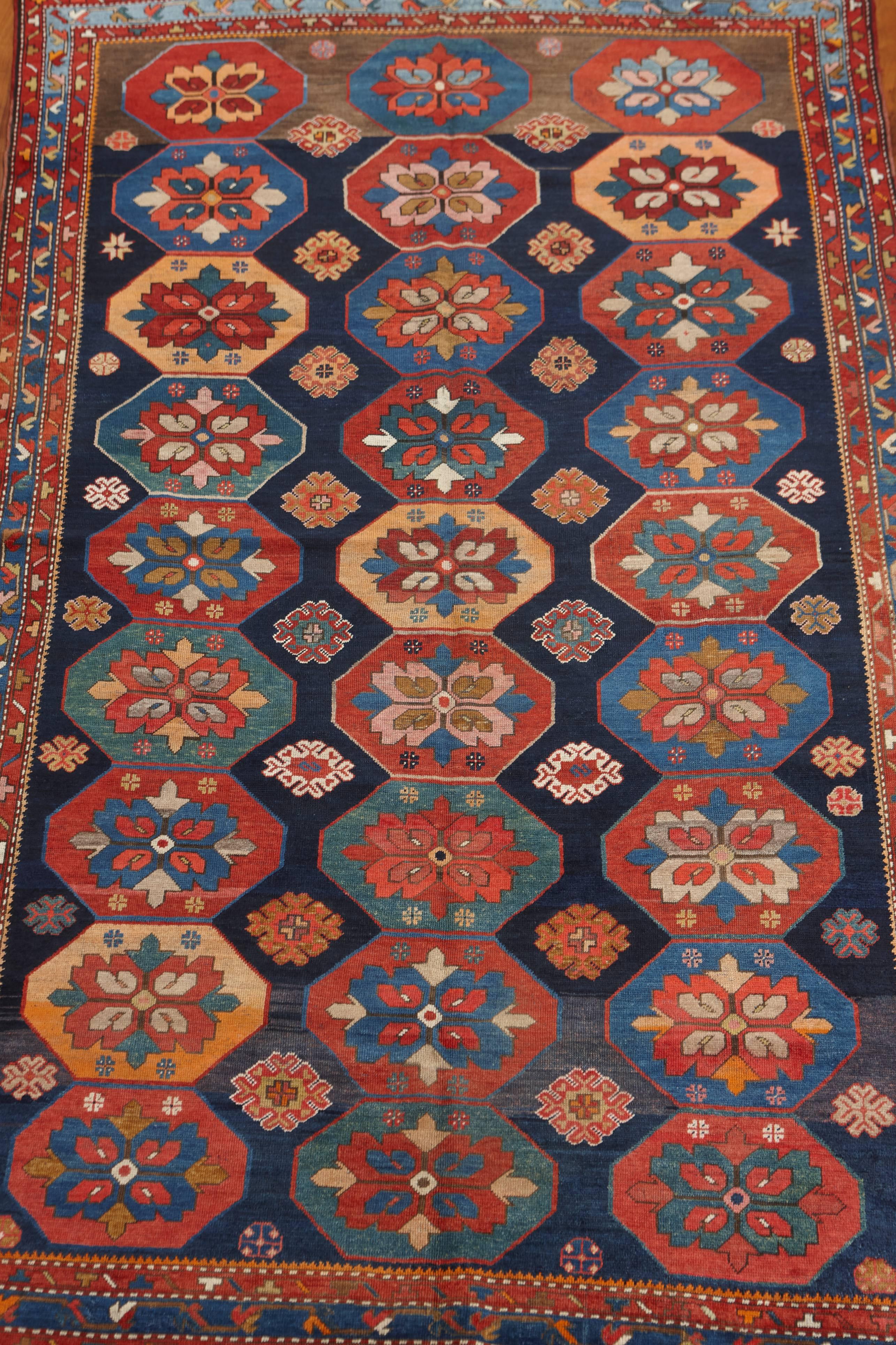 A field of polychrome octagonal medallions are lined along the midnight blue background of this Karabagh rug. Each octagon is inscribed with flowers and four mini-rosettes on its ends. The rug is characterized by rare abrash tonal changes at both of