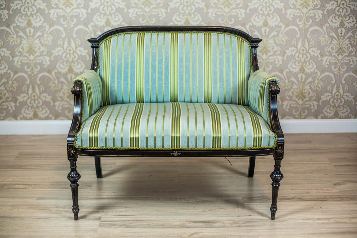 We present you this small two-person sofa in the bergère type, circa third quater of the 19th century.
The sofa has a softly upholstered seat and backrest.
The armrests are padded with a fabric in sky blue-green-golden lines.
This piece of