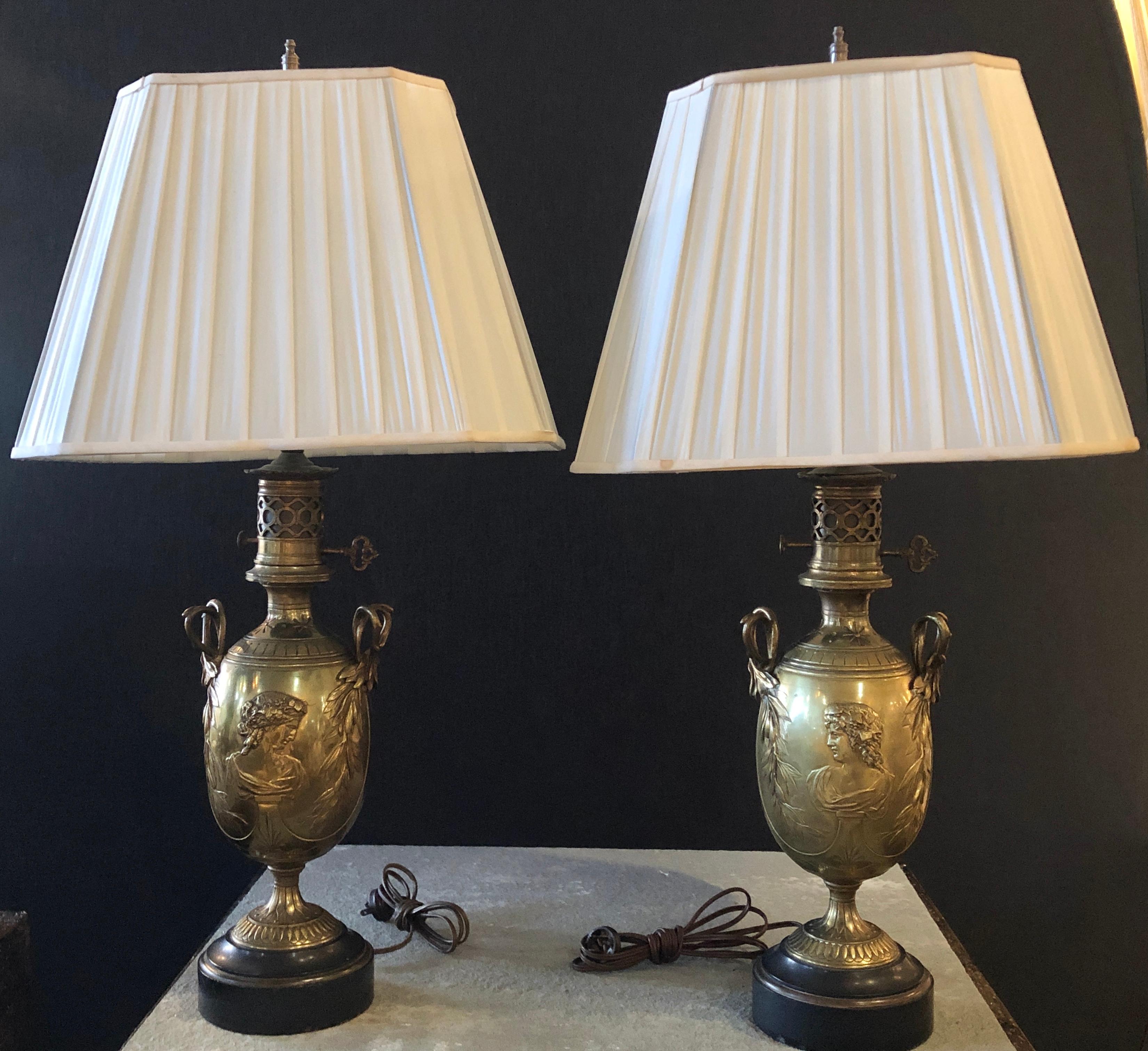 19th century urn shaped Grecian doré bronze table lamps. A pair of stunning oil converted table lamps depicting opposing female busts having fine details with flowing hair and shape. The reef inspired twin handled lamps show the style and flair of
