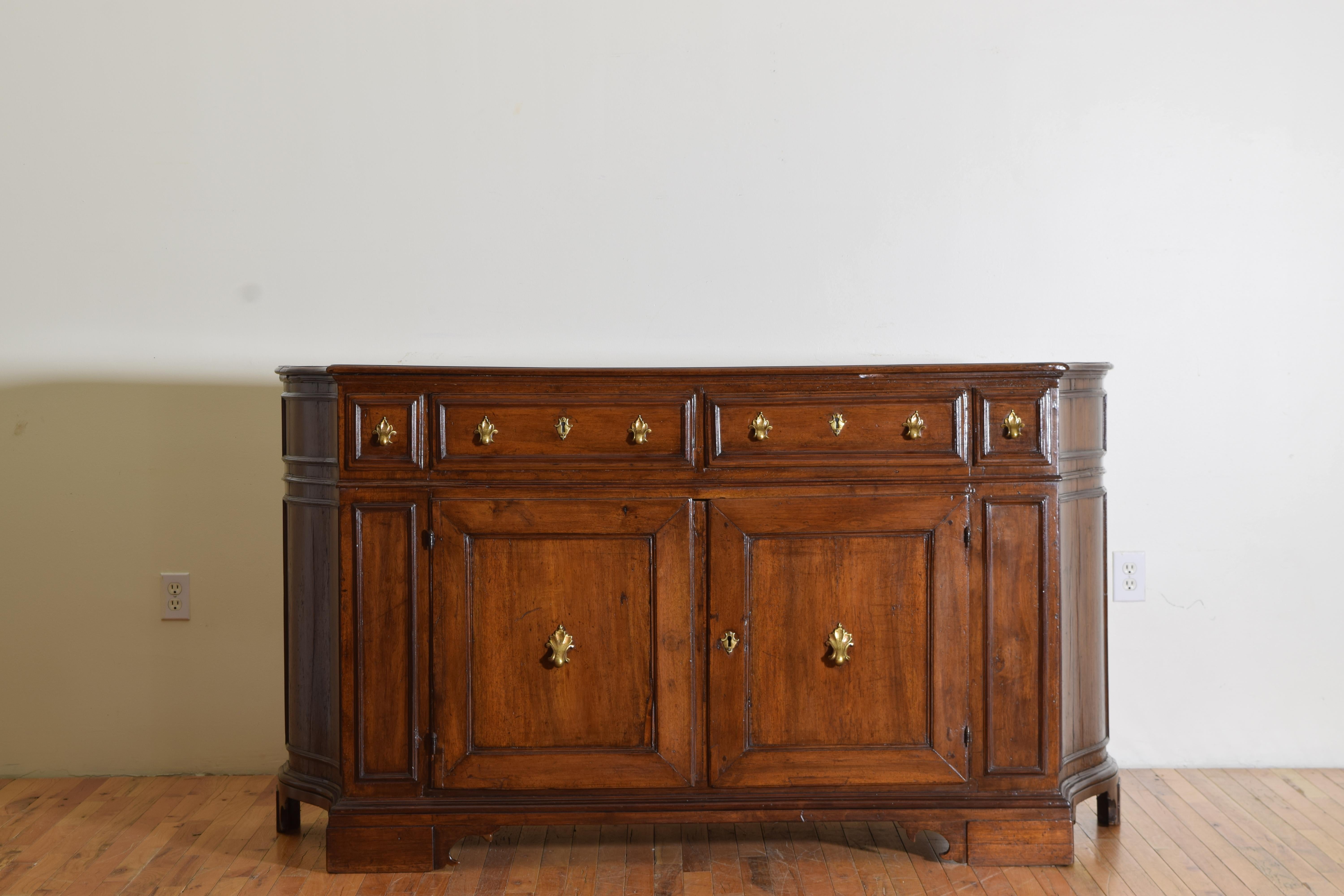 This walnut credenza has three drawers over two doors with elaborate brass decoration for the handles and pulls. The top shaped with a molded edge while the case is also shaped and having molded panels on the doors and sides.