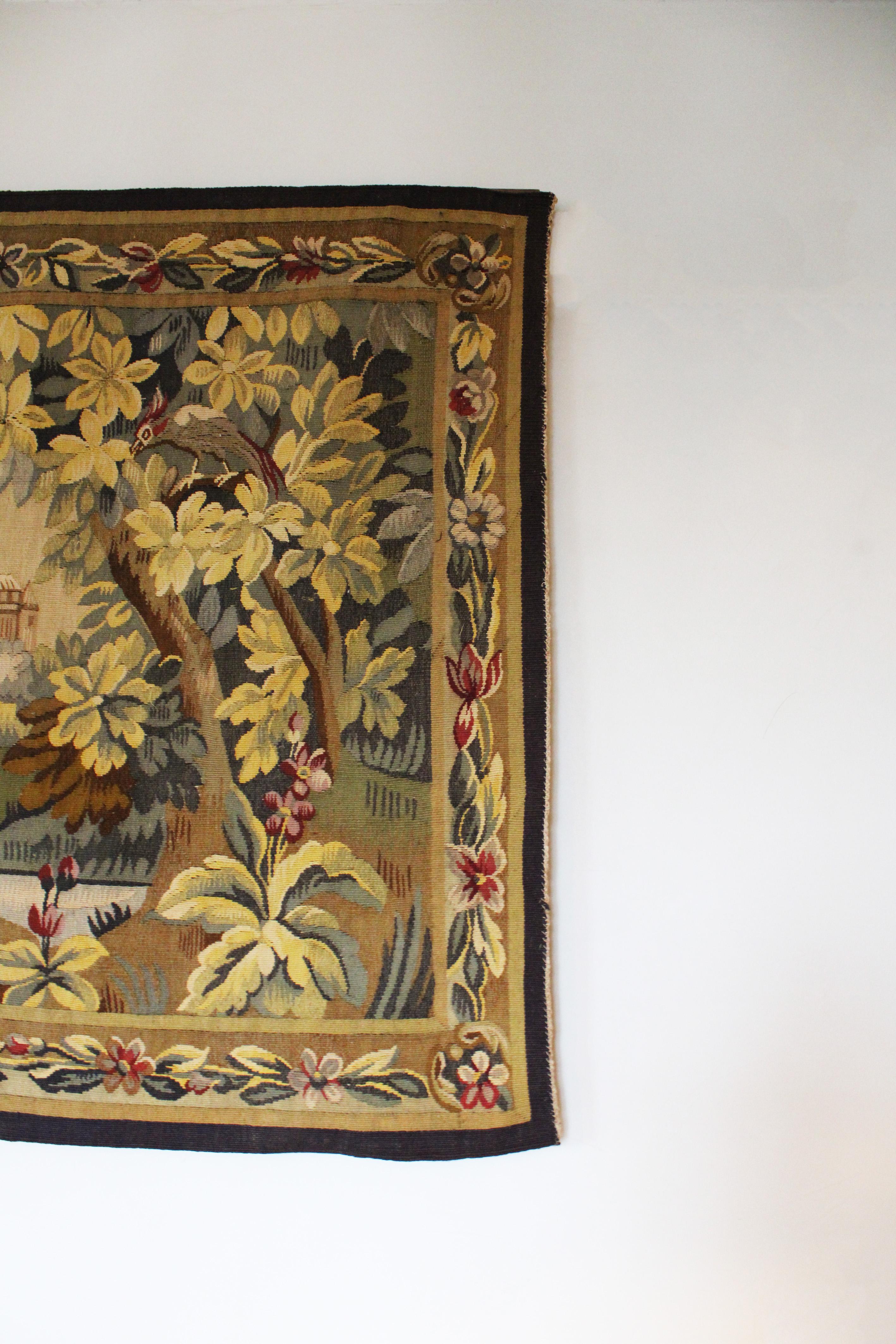 Immerse yourself in the serene beauty of the French countryside with our exquisite 19th Century Verdure Tapestry, depicting a bucolic landscape complete with a river, castle, birds, and blooming flowers. Crafted by Aubusson in France, this wool