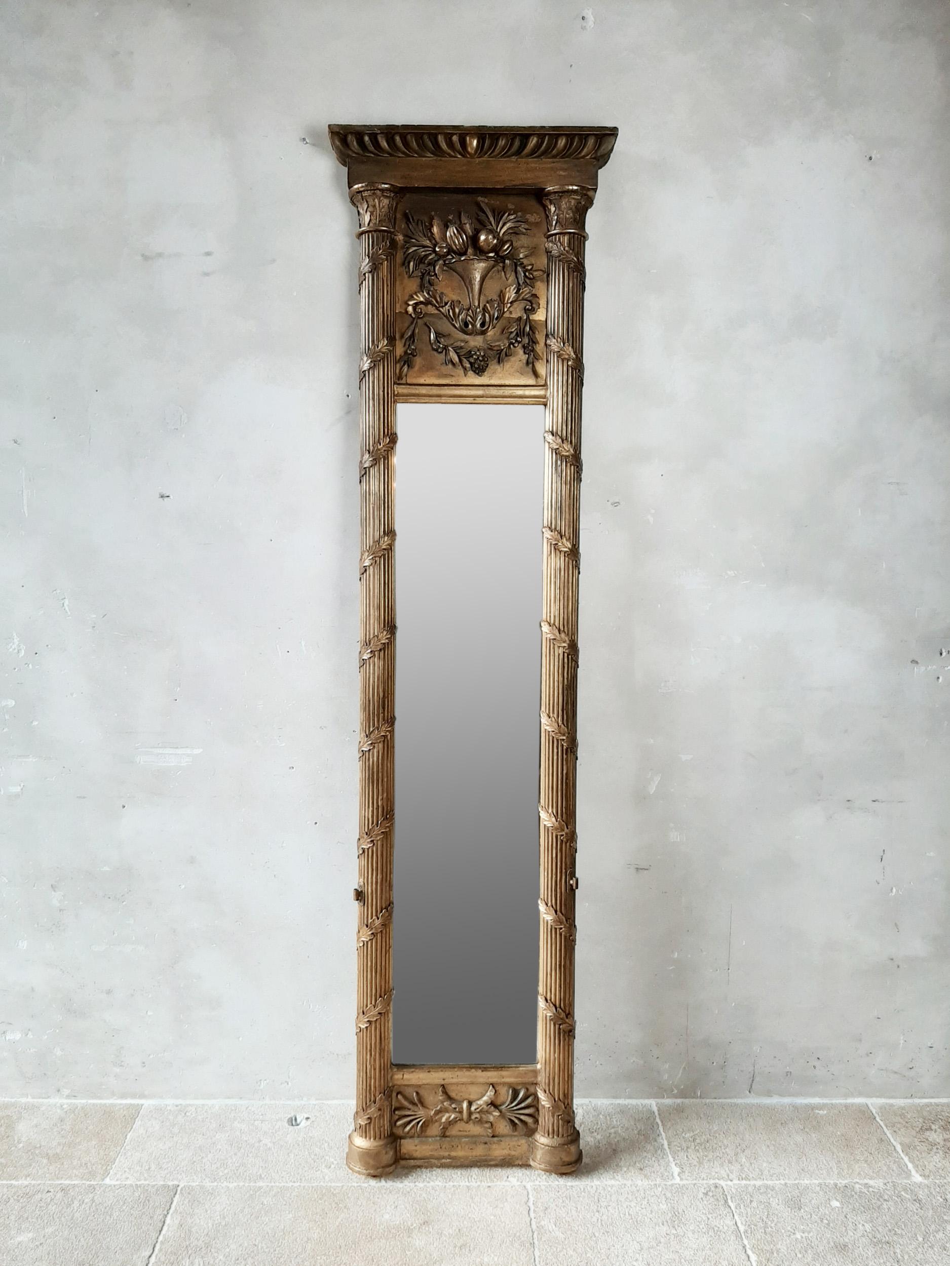 19th century very high, narrow pennant giltwood mirror in Empire style. A mirror that is ideal for use between two windows due to its size. Very rich version with semicircular columns with fluting and capitals decorated with gesso leafs. At the top