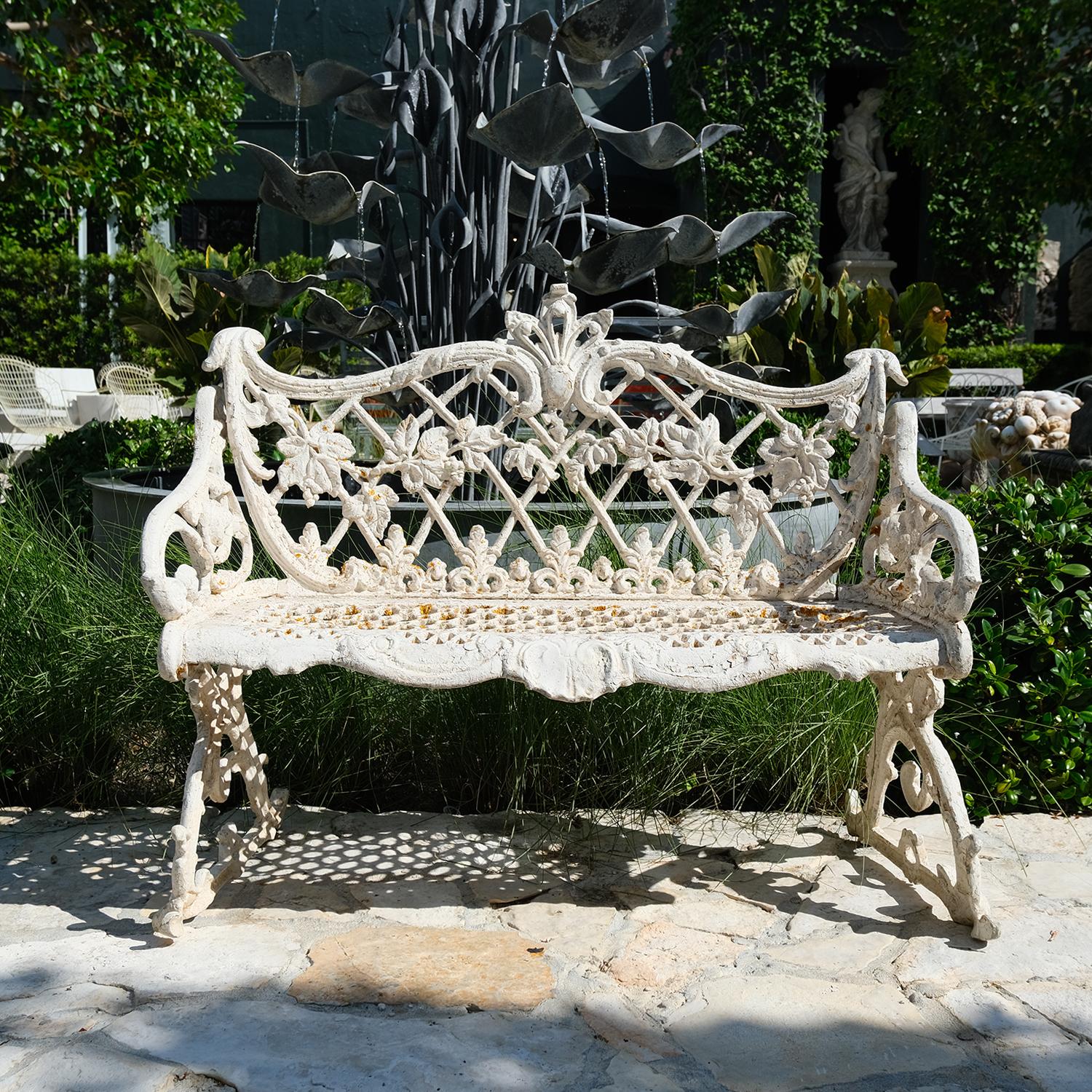 Antiguo banco de jardín inglés victoriano de hierro fundido con diseño de volutas, decoración de hojas y motivo centrado en el asiento y el respaldo, en buen estado. El asiento está perforado, con una pátina blanca. Pequeña decoloración, arañazos