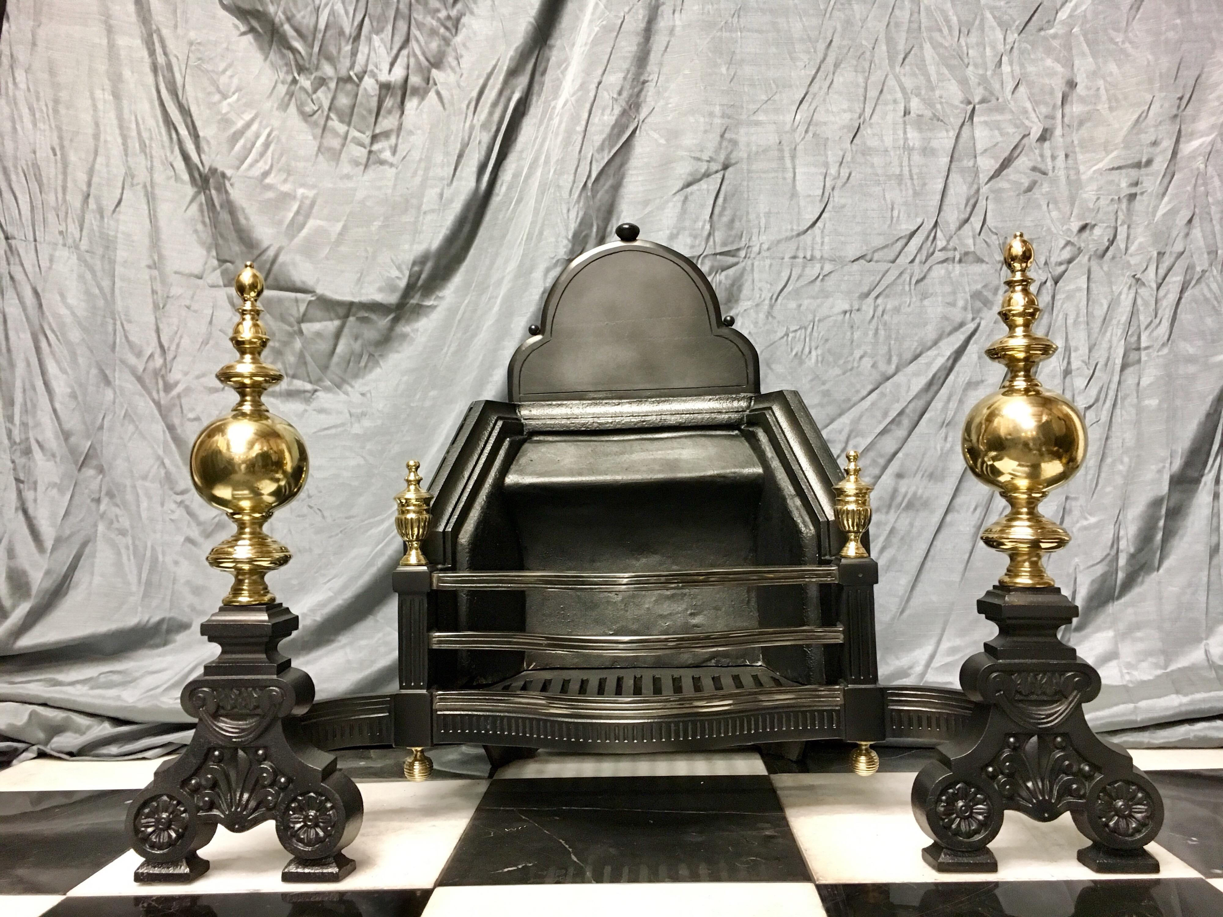 A large Baroque style cast iron Victorian fire basket with a shaped fire back, a two barred serpentine shaped grate mounted with a pair of brass Urn finials supported on large scrolled feet with tall brass baluster standards.

English, circa