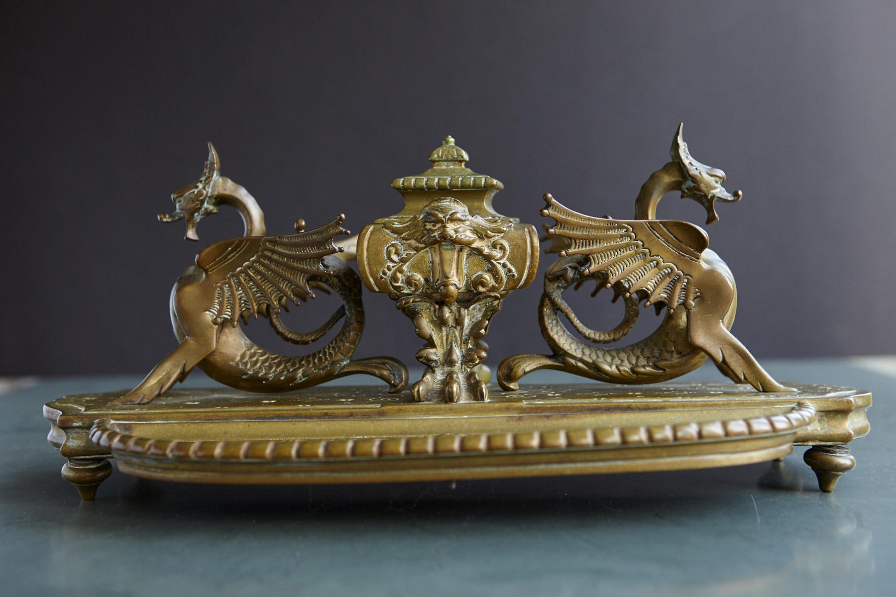 Impressionnant, grand encrier victorien en laiton du XIXe siècle accompagné de chaque côté de dragons ailés à queue serpentine. L'encrier est équipé de pieds griffes et d'un couvercle à charnière. Un porte-plume avec des motifs défilants en relief