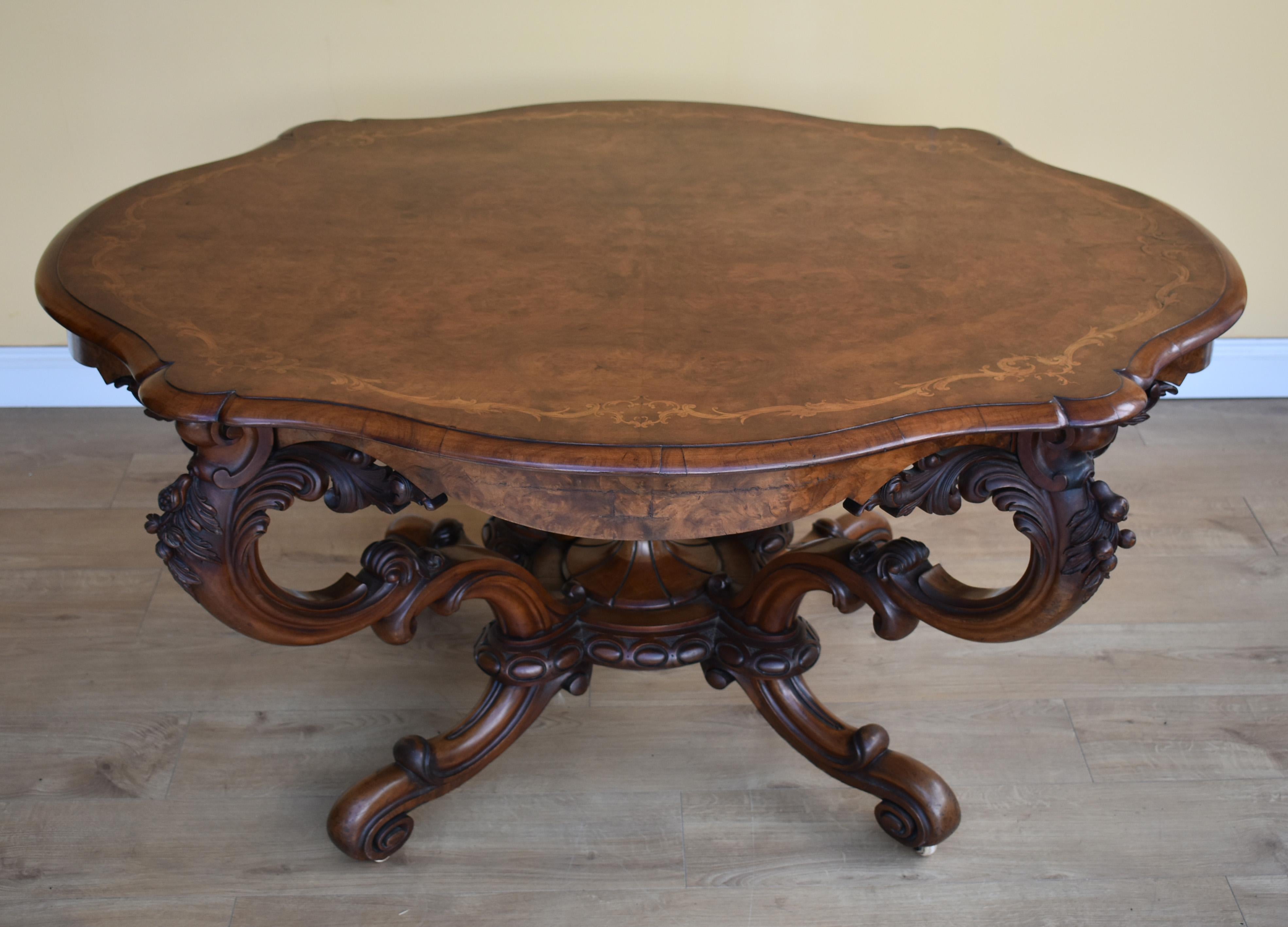 For sale is a fine quality Victorian burr walnut and marquetry inlaid table. The top is ornately shaped and has scrolling leaf inlay to the edge, this is supported by four intricately shaped and carved legs with a finial in the centre. This table is