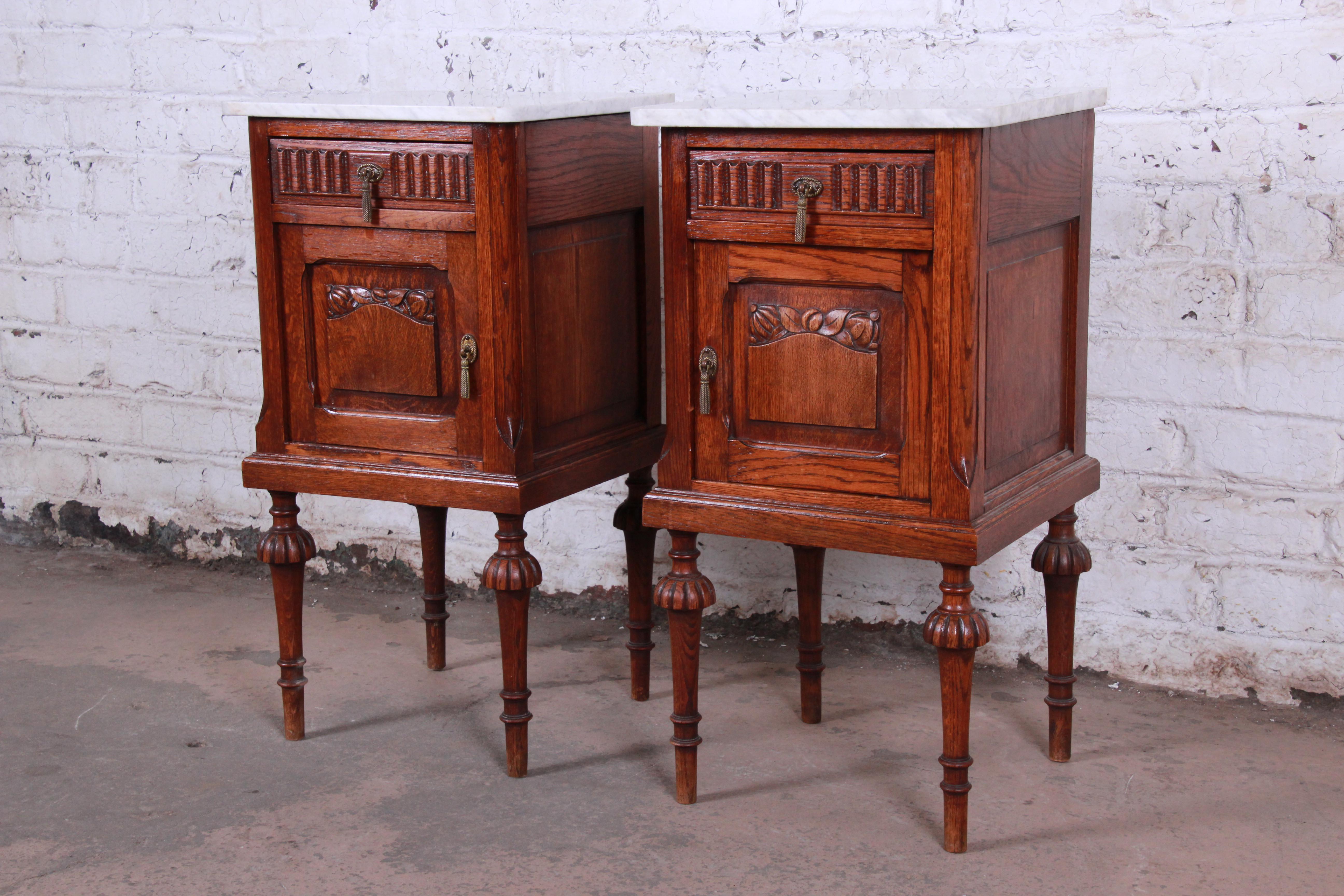 An exceptional pair of 19th century Victorian carved solid oak nightstands. The nightstands feature gorgeous oakwood grain with nice carved details and beautiful white marble tops. They offer good storage, each with one dovetailed drawer and