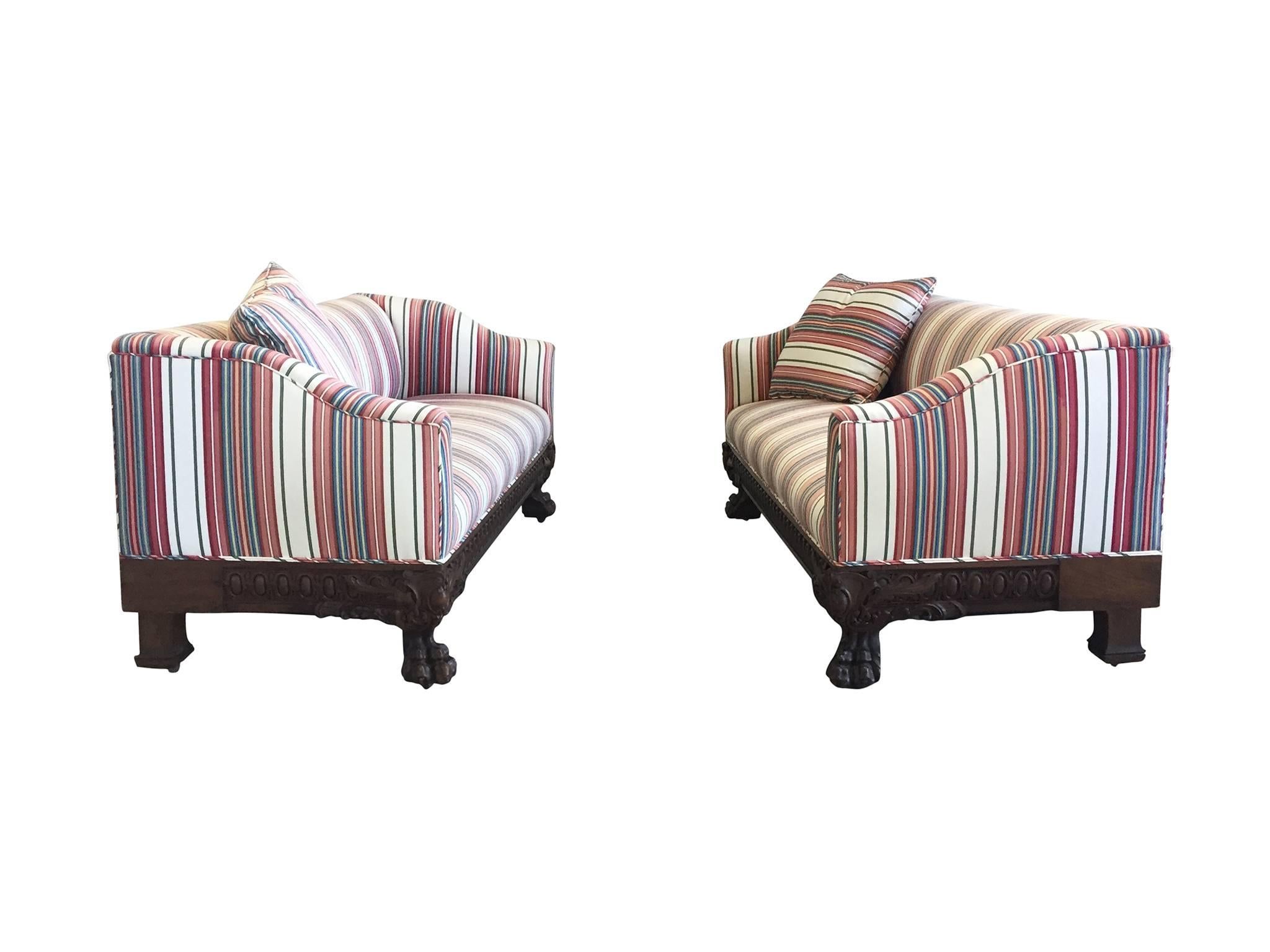 These two sofas were made in the 19th century. They are of the Victorian era. The design consists of a low back which slopes gently into the arms. The wood base are elaborately carved at the front which culminates in monopodium feet featuring a