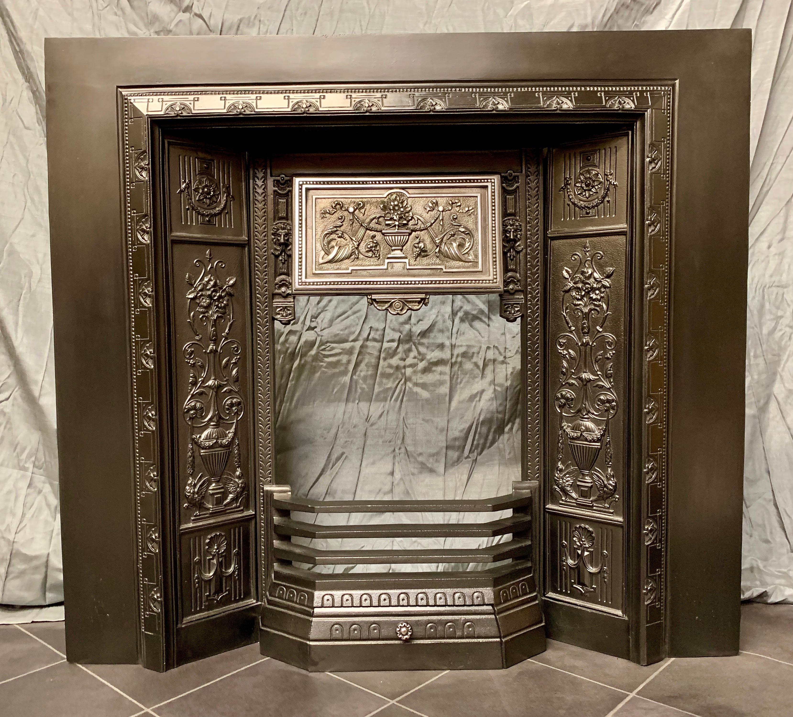 A charming and ornate 19th century Victorian cast iron fireplace insert with exquisitely cast side panels and a polished fire hood showing a central urn flanked by Cornucopia and bell flowers and swags. A generous sized piece that is stamped with a