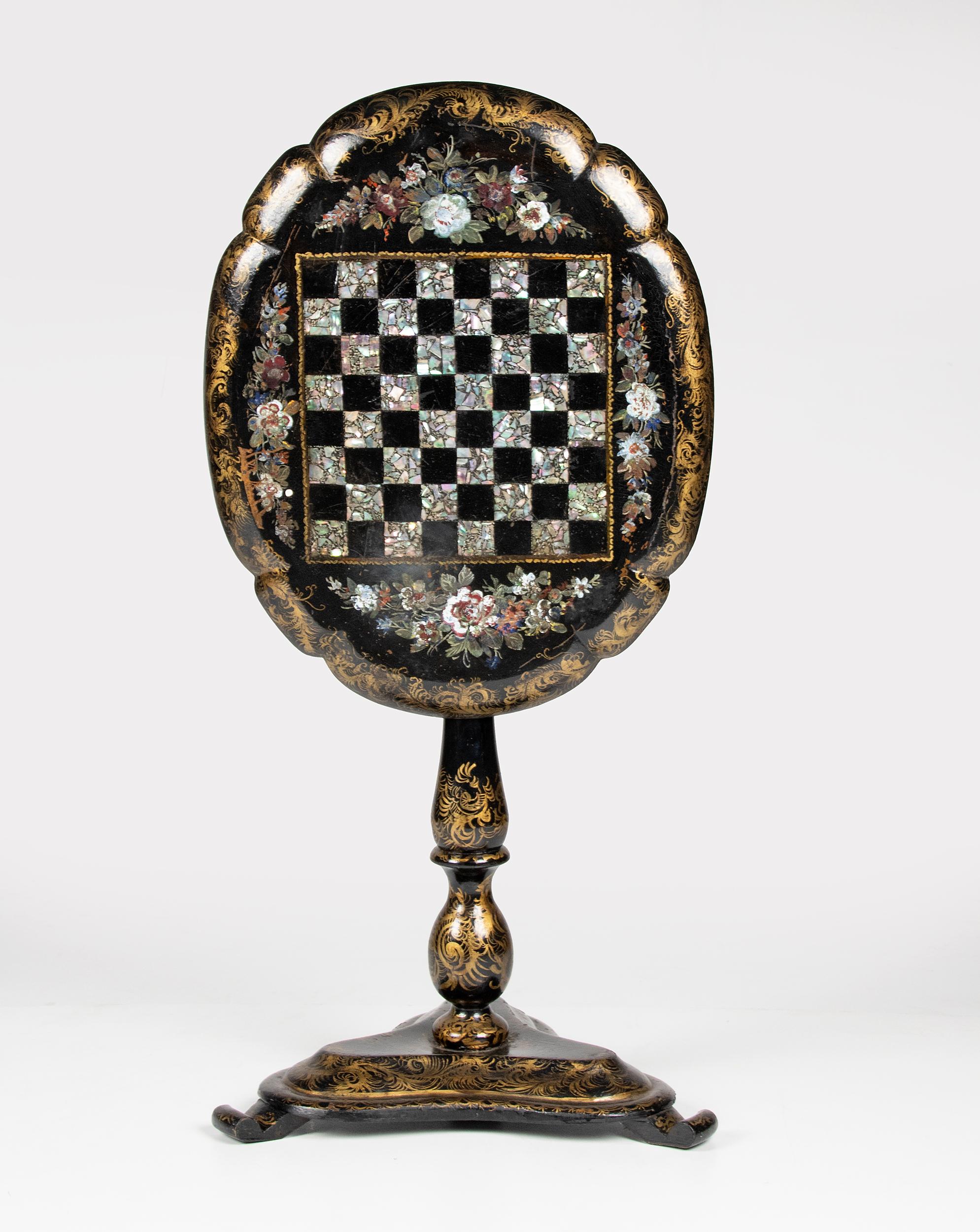 Beautiful Victorian chess table. It is a tilt top model, the top can be folded up. The table is made of black lacquered wood and papier mâché. It is inlaid with delicate pieces of mother of pearl and painted with floral and gold decorations. The