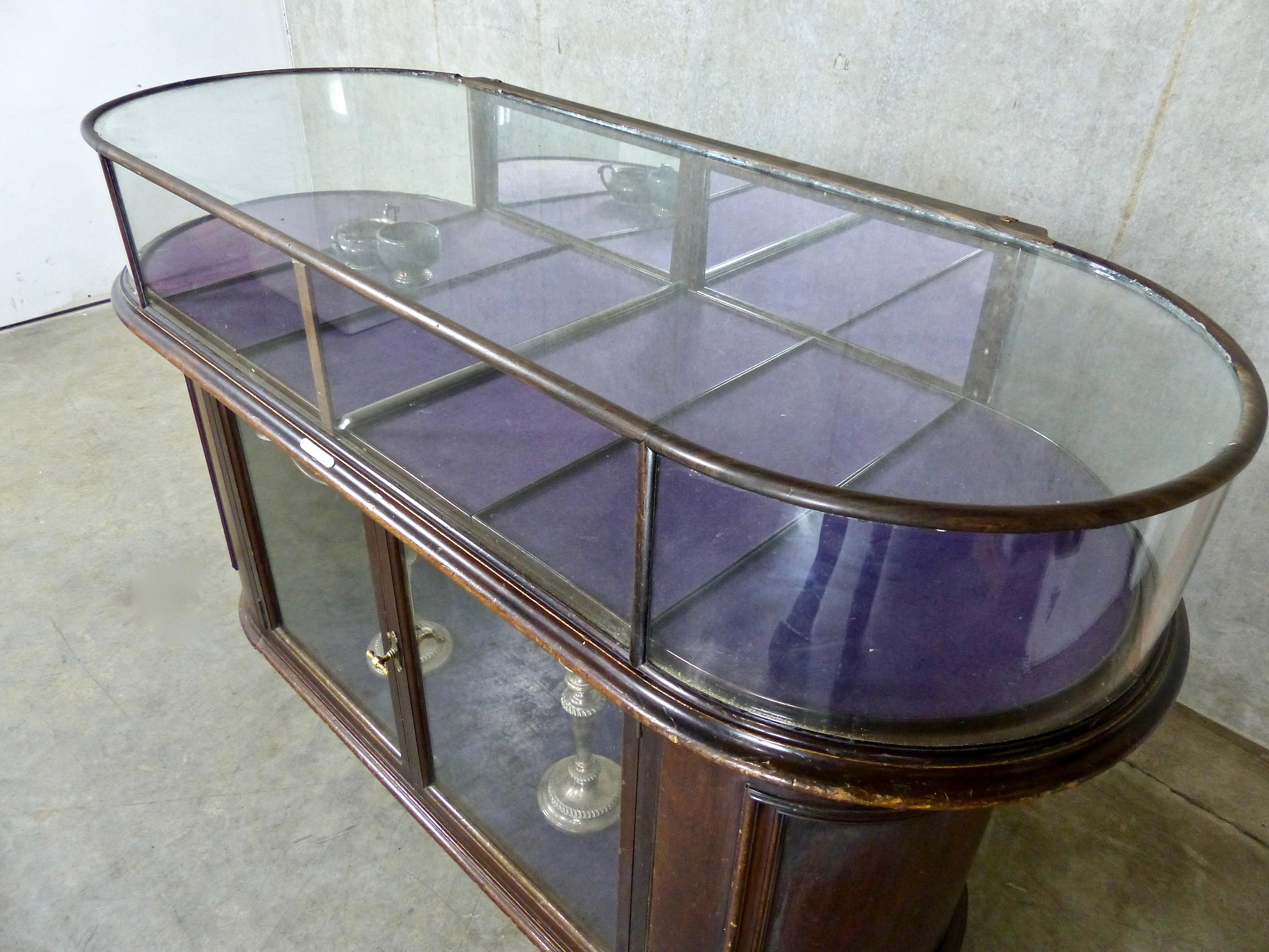 A beautiful curved glass and mahogany mercantile cabinet, circa 1900, made by John Curtis and Son Shop Fitters, Leeds, England. It was likely designed to display jewelry and silver ware as it includes six removable, purple felt-lined trays. The