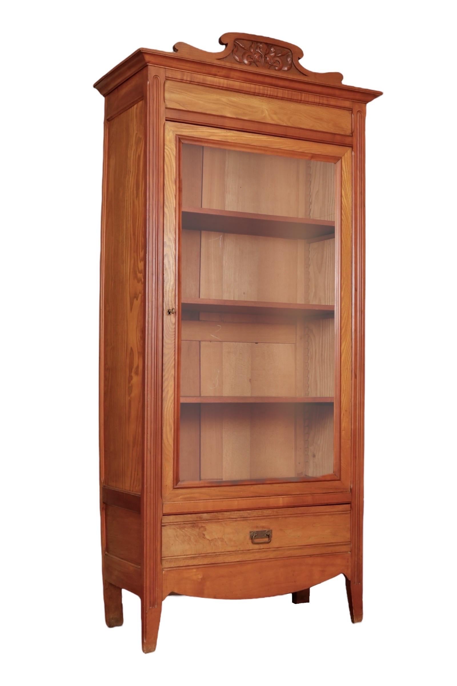 A 19th century cabinet with a locking glass door. The top pediment is carved with scrolls and acanthus leaves above a beveled cornice. Front shoulders are decorated with fluted columns that continue down to straight legs. The cabinet houses three