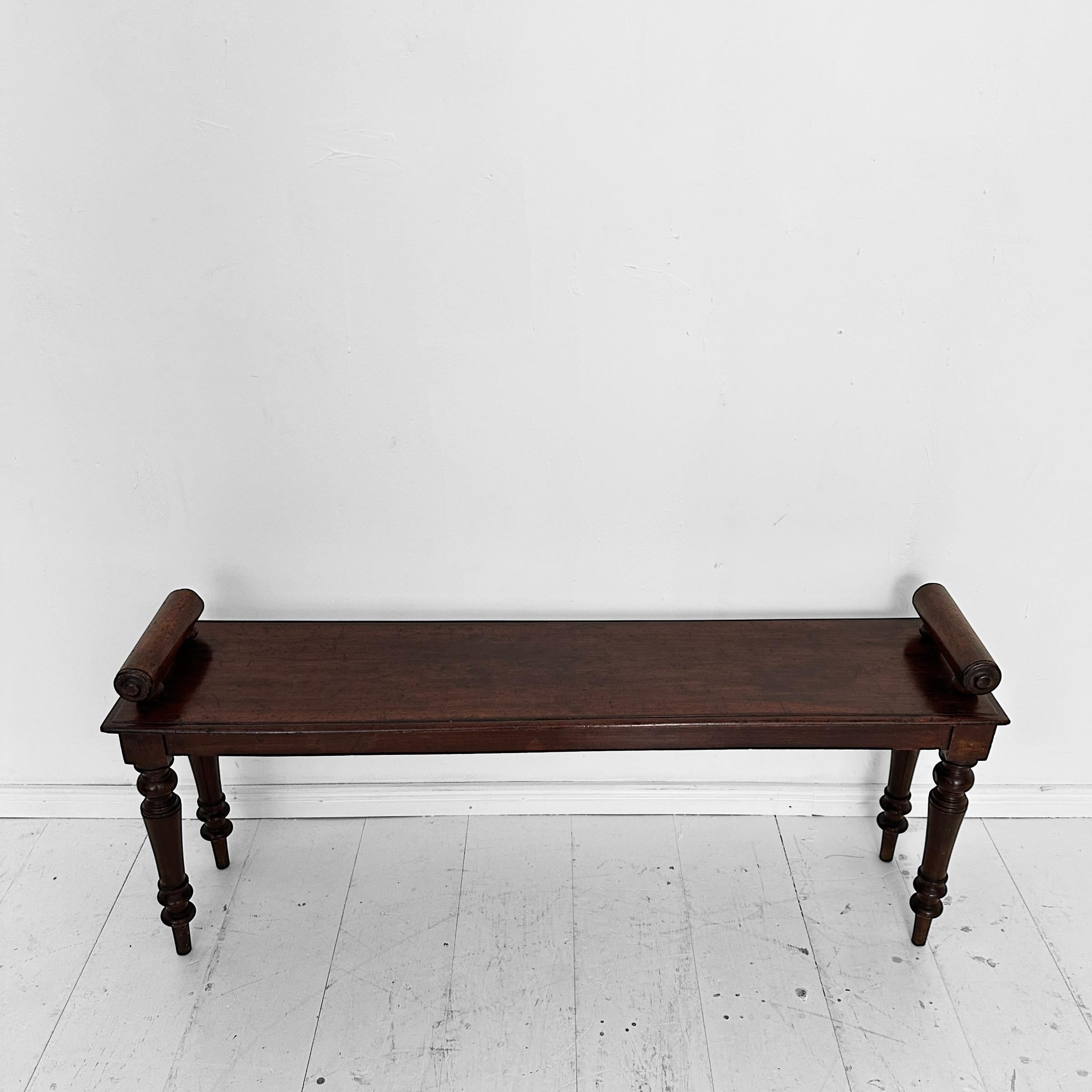 Questa panca da ingresso vittoriana del XIX secolo, realizzata in Inghilterra intorno al 1870, è un esempio straordinario di artigianato d'epoca e design raffinato. Realizzato in un ricco legno rosso-marrone, presenta quattro gambe tornite con i