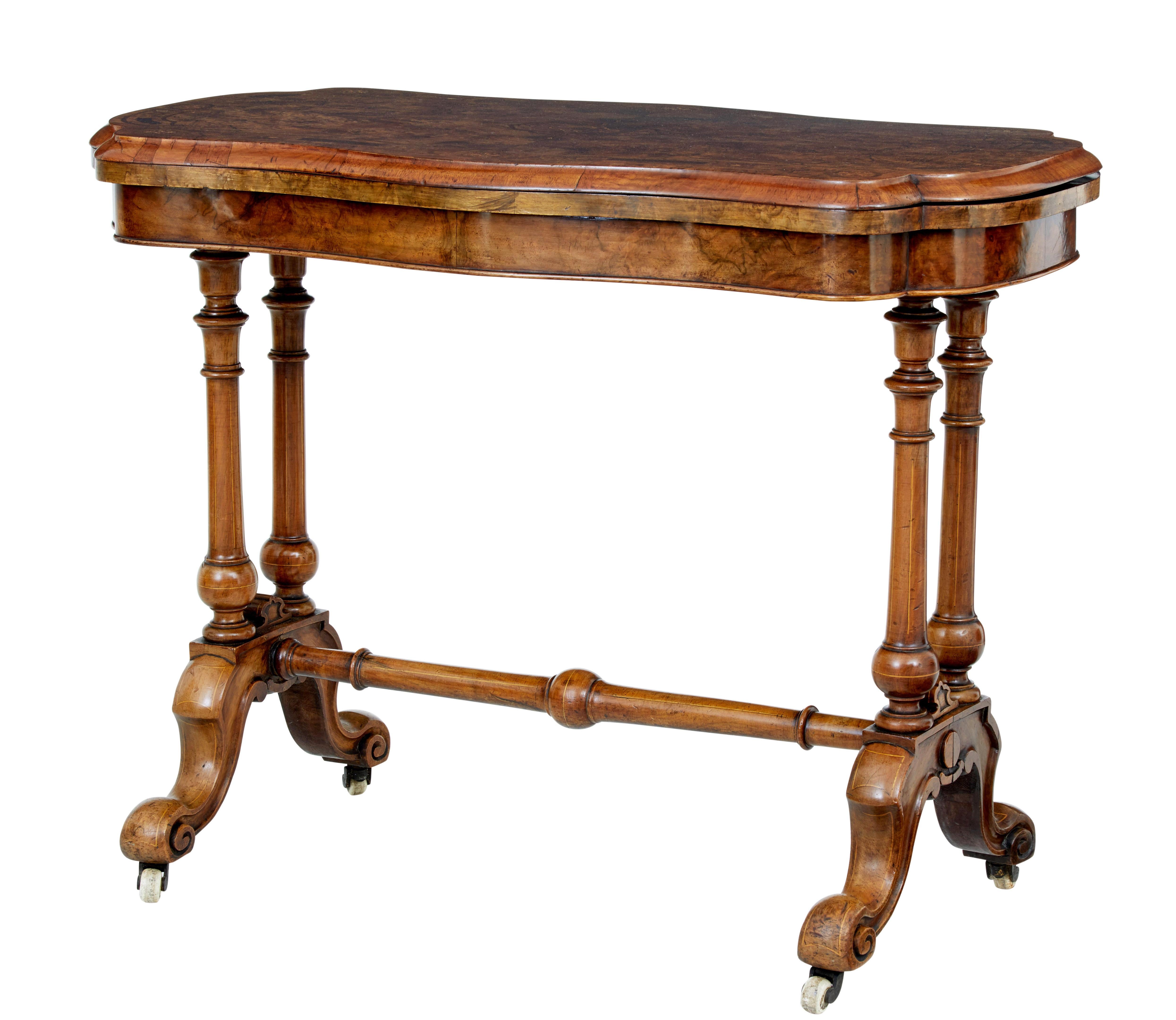 Tavolo da gioco decorativo in noce di epoca vittoriana, circa 1870.

Piano sagomato in radica di noce con motivi intarsiati e decorazione a fasce incrociate.  La parte superiore è girevole per rivelare un vano portaoggetti e si apre su una