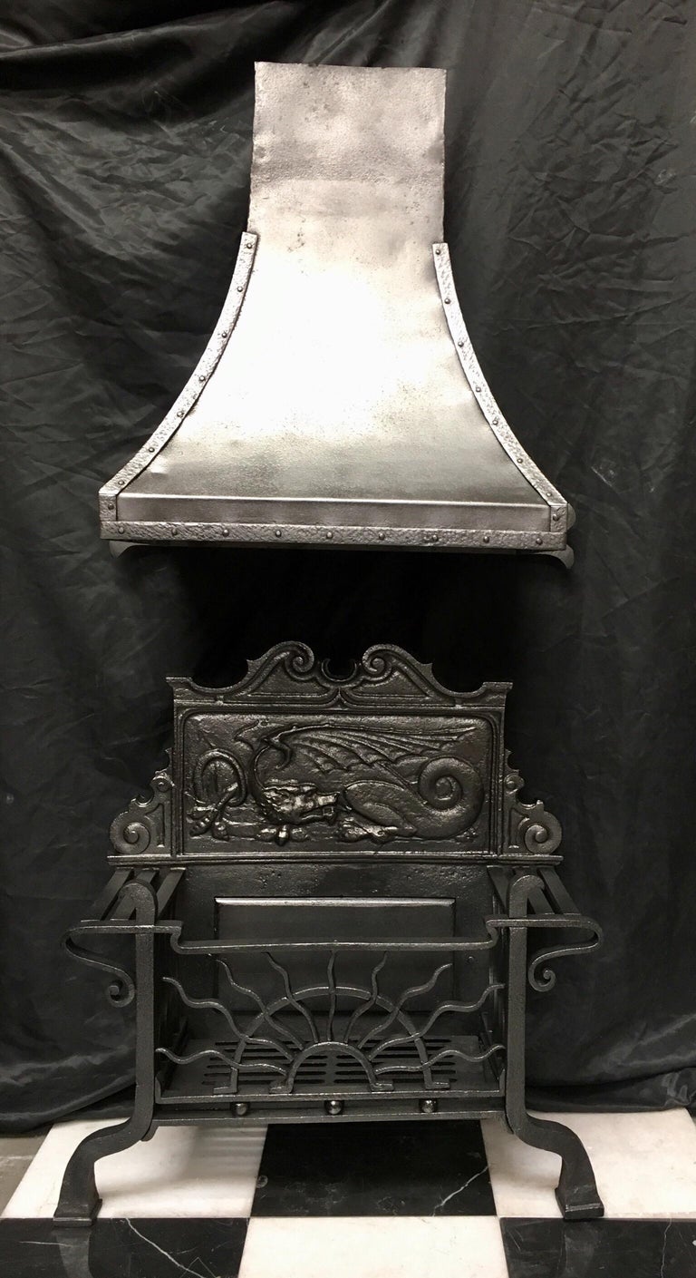 An original antique 19th century -Victorian wrought iron fire grate basket in the Aesthetic Manner with its original sweeping chimney hood. A high Cartouche shaped fire back with a central stylised Dragon set within a cast frame, supporting side