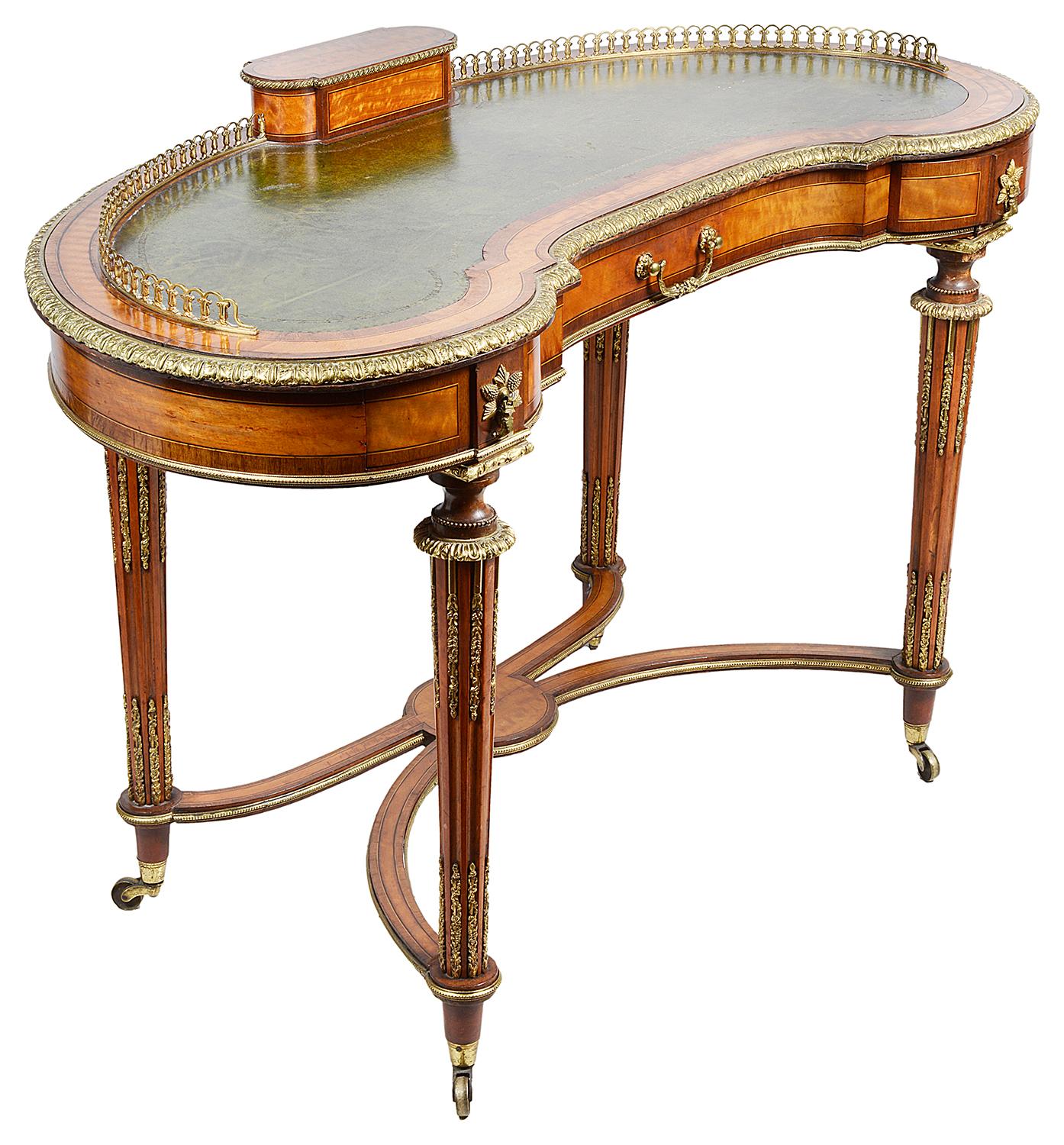 A very good quality Victorian period satinwood kidney shaped ladies writing table, having scalloped gilded ormolu three quarter gallery, a hinged pen tray and letter rack to the centre, an inset leather top, three mahogany lined frieze drawers,