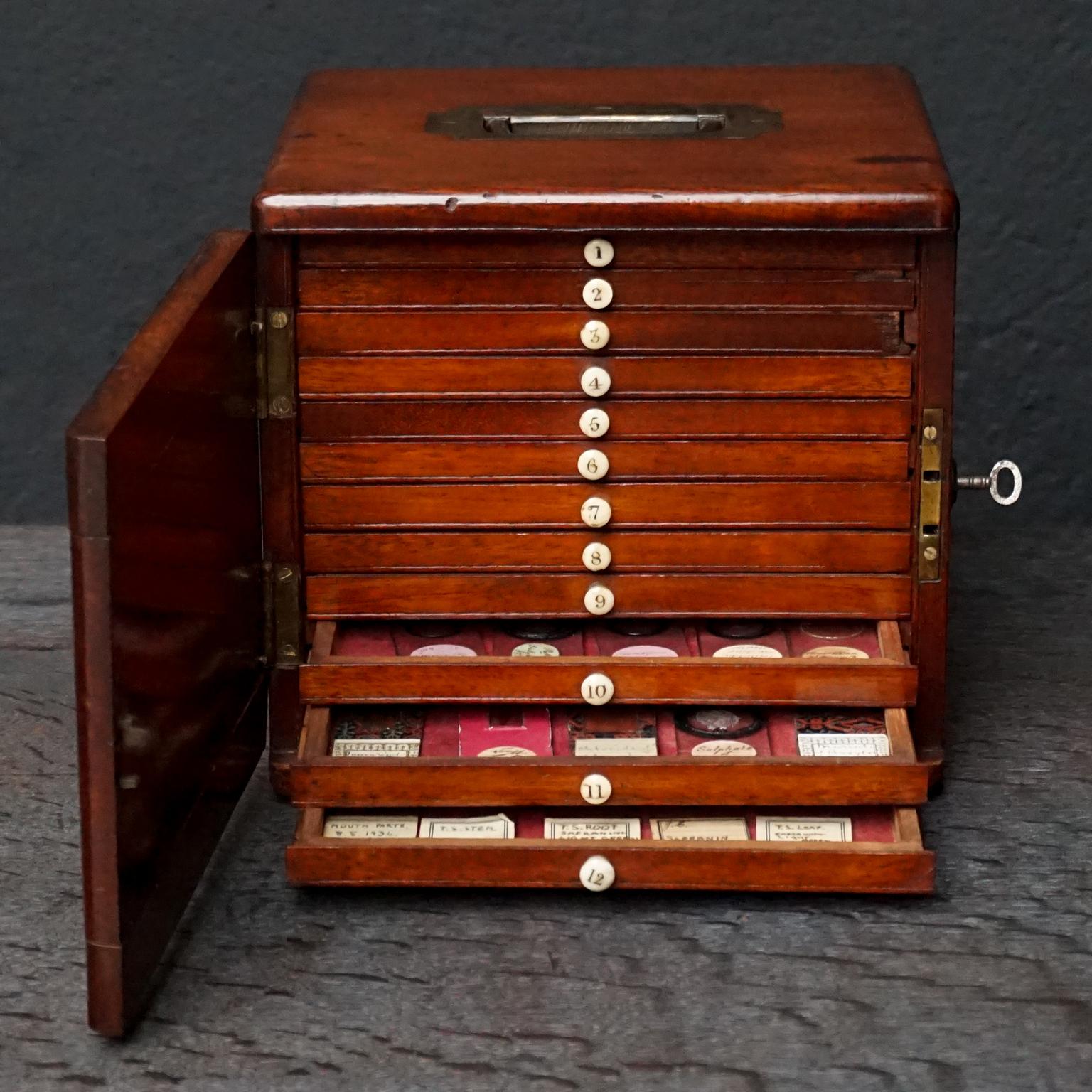 Cute little square English Victorian mahogany 12 slide cabinet with 72 microscope slides. 
With brass carrying handle, closes with original key and lock on the right side of the box.
Containing 12 little drawers lined with red velvet, each with a