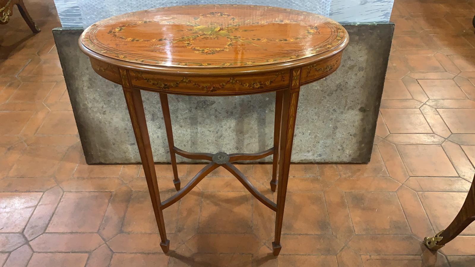 Elegant Satinwood oval tray table, painted with floral scenes and musical triumph, top with oval glass tray, four pyramidal legs connected by crosspieces. England second half nineteenth century.
