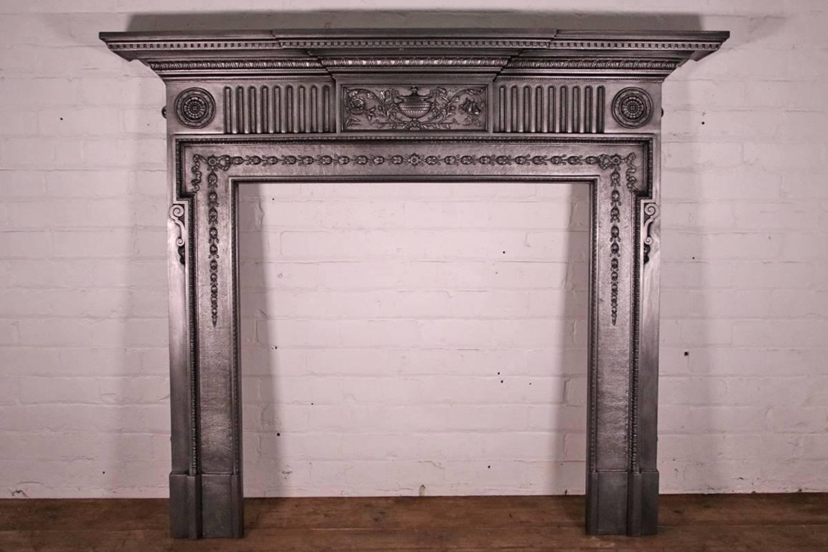 19th century Victorian cast iron fireplace surround in the neoclassical design. The break fronted mantel sits above a fluted frieze with a central tablet cast with fine detail of a classical urn surrounded by flowing branches and flowers. The under