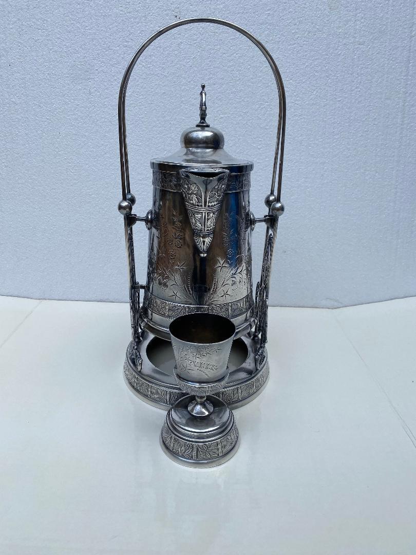 Brocca per bevande in argento quadrupla Pairpoint del XIX secolo con supporto e calice.
Presenta un motivo floreale e di foglie in rilievo.  
Piedistallo con supporti forati; timbro sulla base del famoso produttore, Pairpoint, Quadruple silver