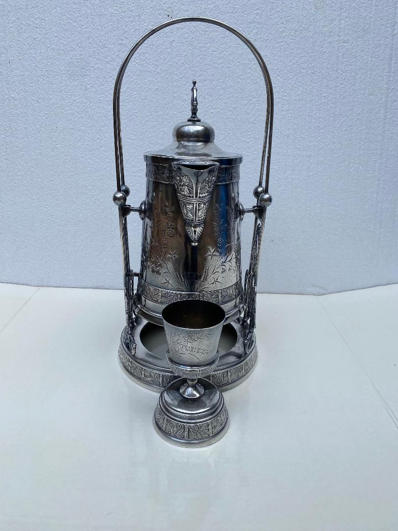 19ème siècle Victorien Pairpoint quadruple silver plate beverage pitcher with stand and goblet.
Il est orné d'un somptueux motif floral et de feuilles en relief.  
Socle avec supports percés ; estampillé sur la base par le célèbre fabricant,