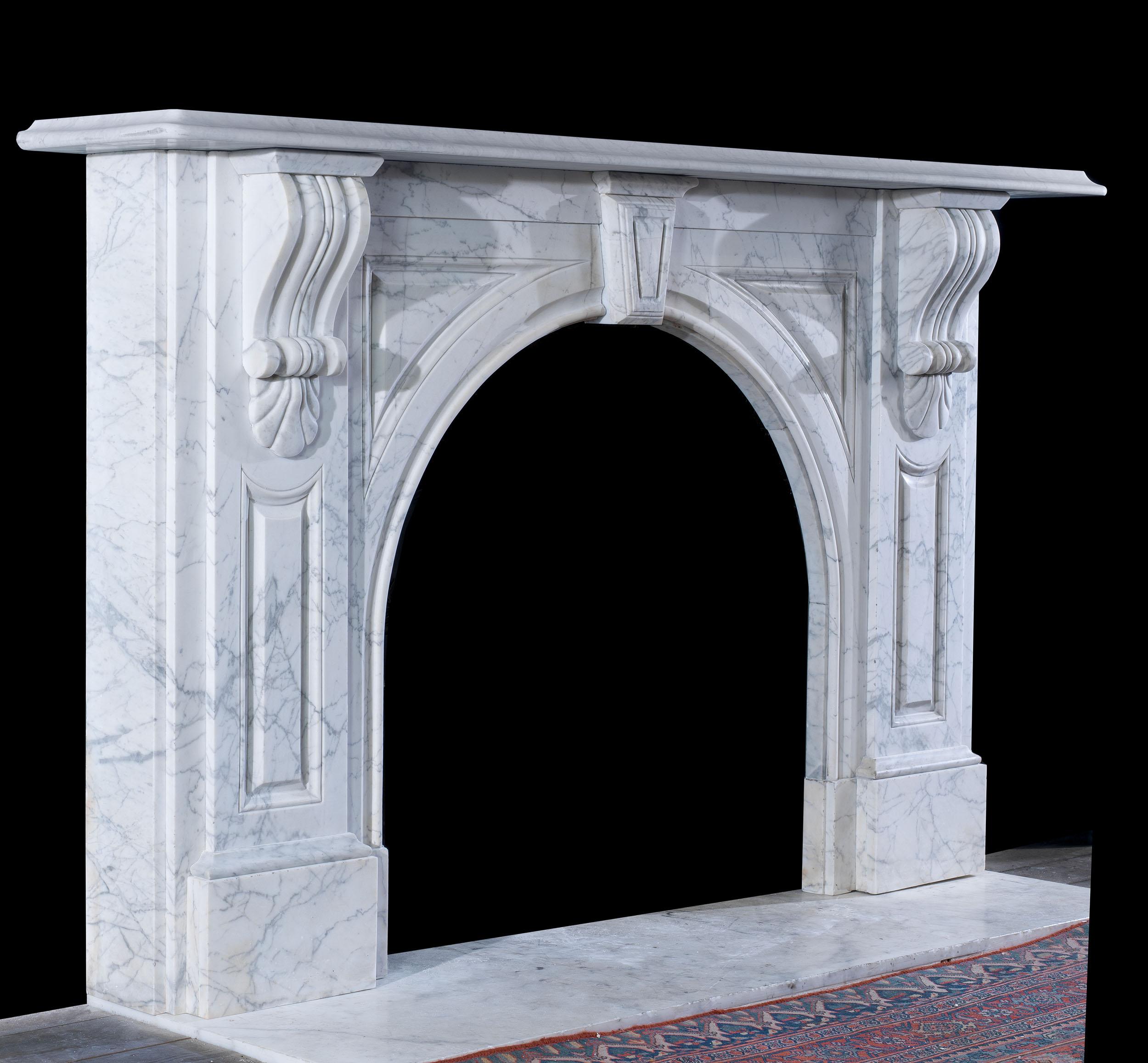 A large Victorian arched fireplace in pencil statuary marble. The fireplace features a wide moulded shelf over an arched opening carved with panelled spandrels. The boldly carved acanthus corbels are mounted on panelled jambs over plain