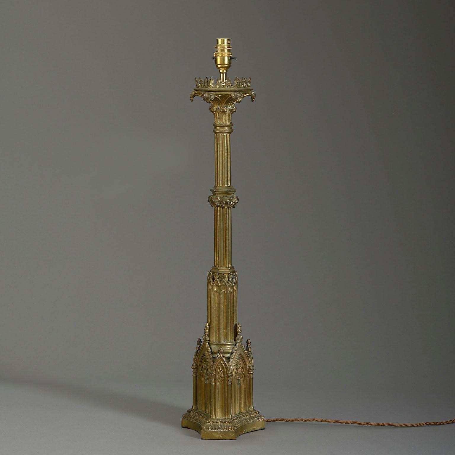 A late nineteenth century brass column lamp in the Gothic taste, the staged cluster column stem set upon a triform plinth base with blind tracery arches.

Dimensions refer to antique brass elements only.

Wired to UK Standards. This lamp can be