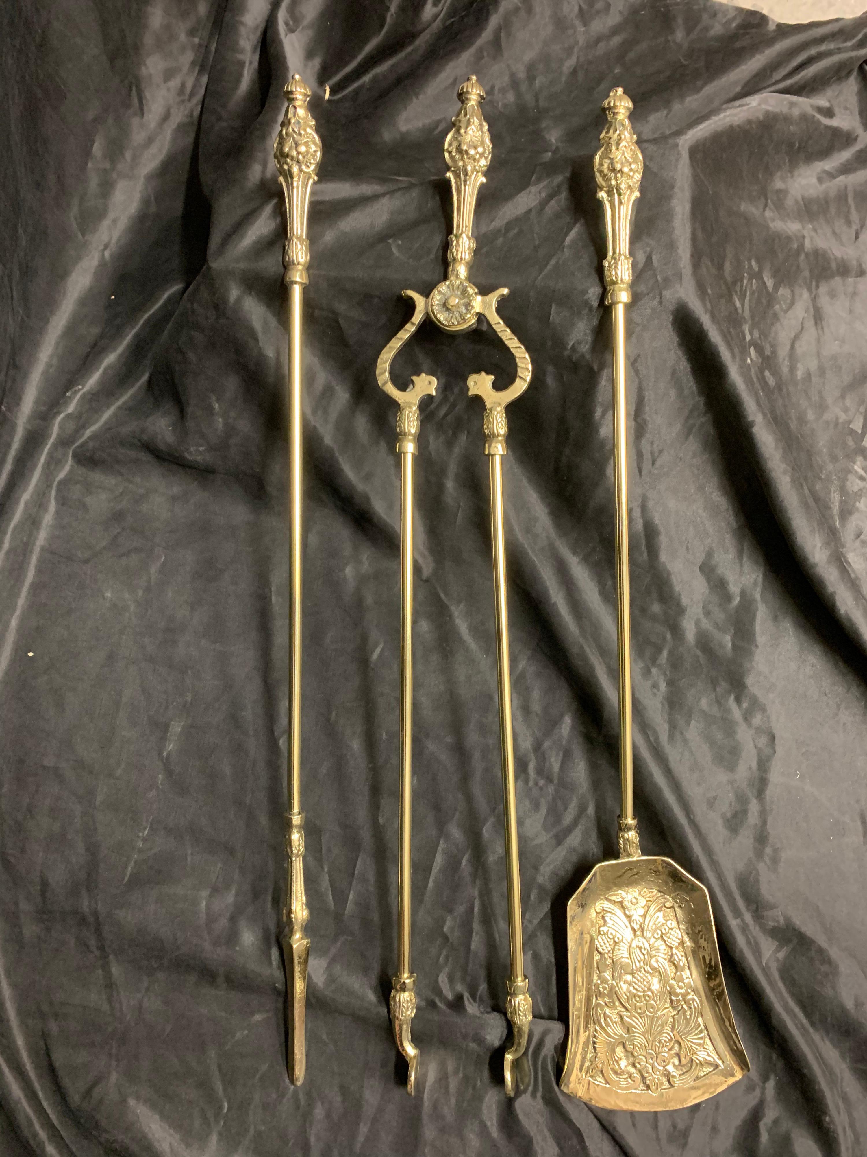A set of three 19th century Victorian polished brass fire iron tools consisting of a poker, a decoratively cast shovel, and a pair of tongs with a snake style hilt, each with an ornate classically cast handle with button top finials.

English